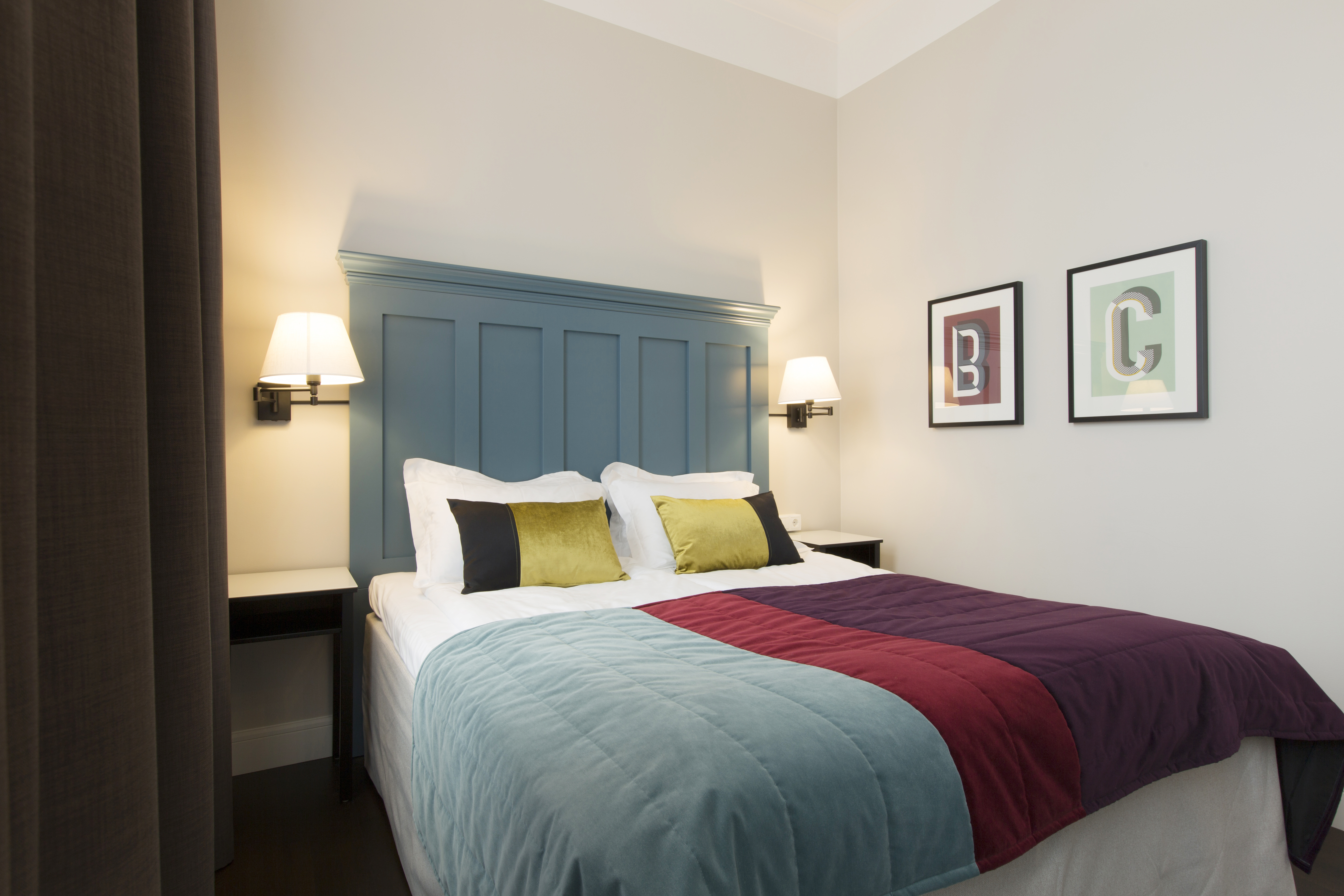 Bright hotel room with bed, large blue headboard and bedside tables