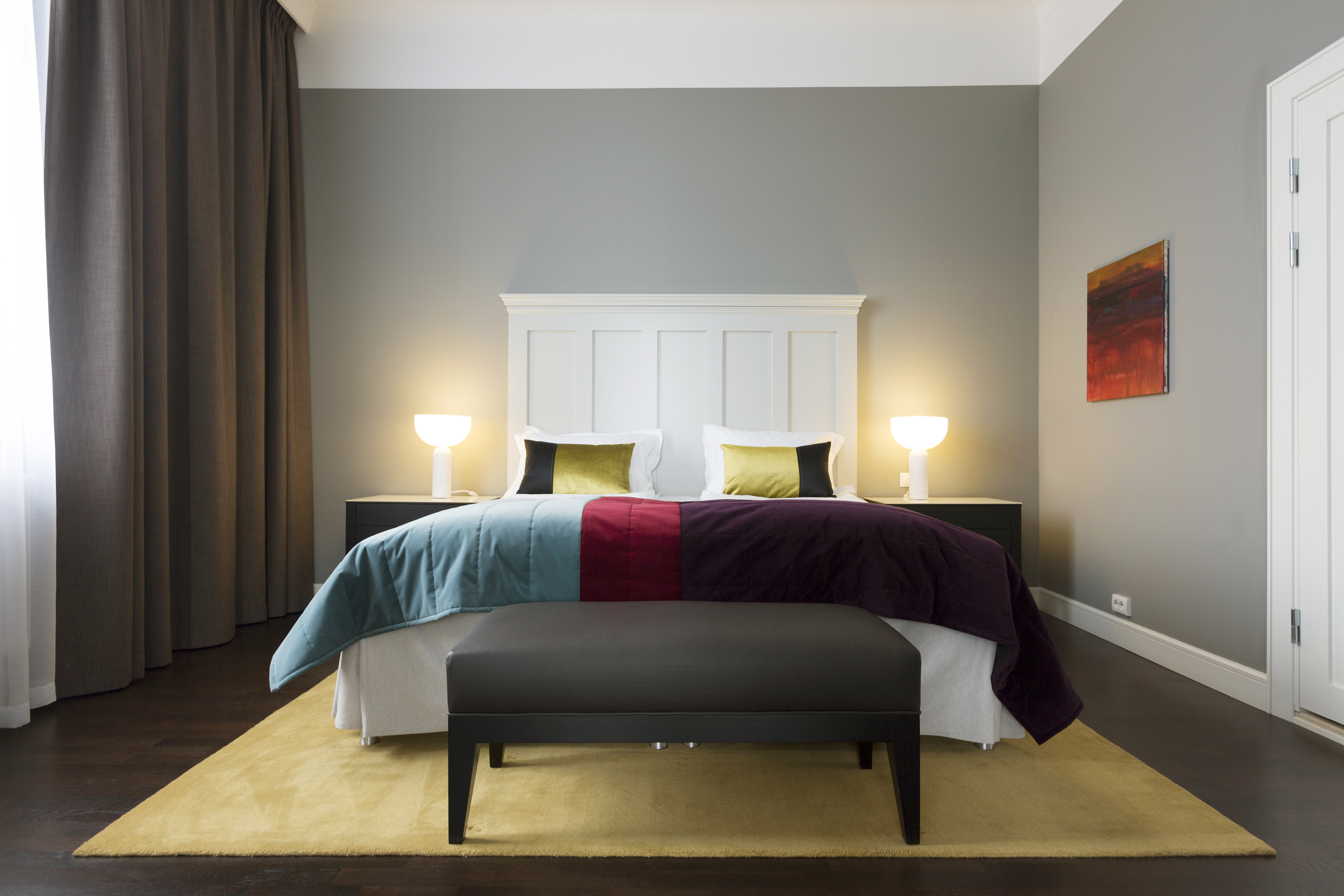 Bright suite with bed, large white headboard and bedside lamps