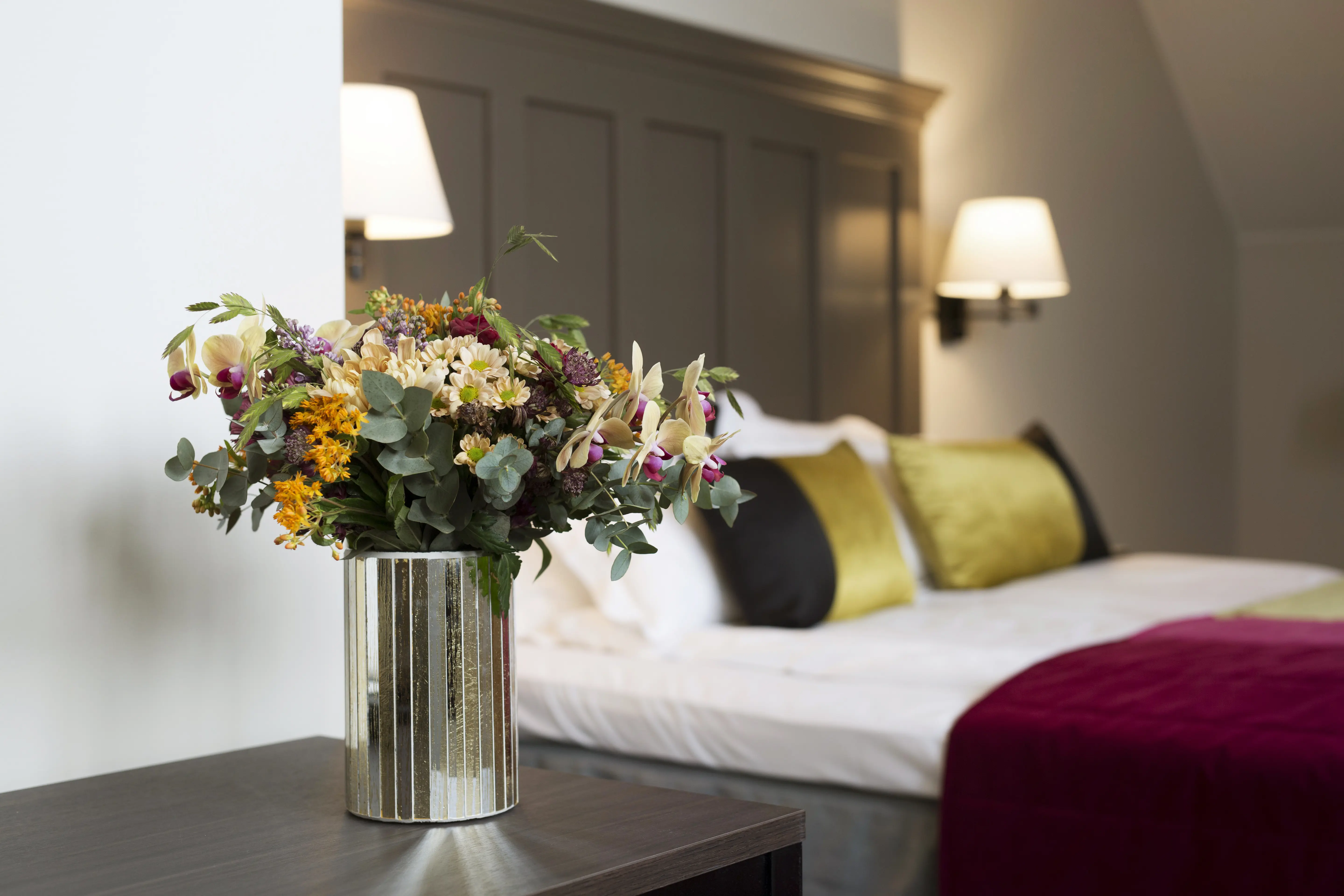 Blombukett i vas framför en bäddad dubbelsäng.