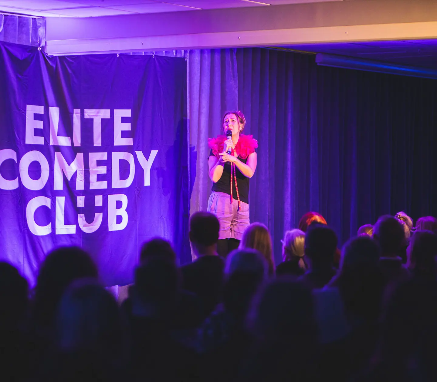 Stand-up-komiker uppträder på scenen vid Elite Comedy Club inför en engagerad publik.