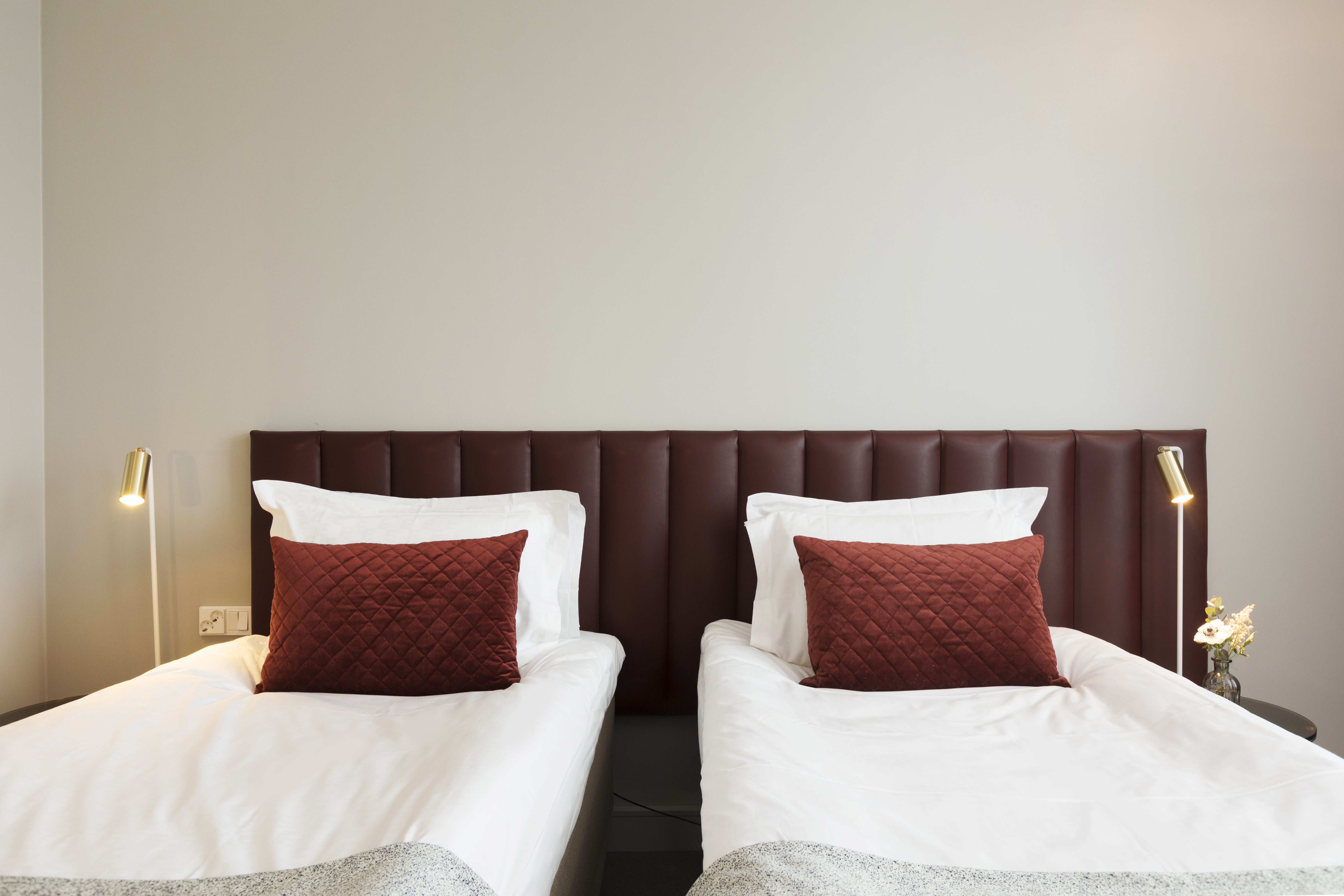 Bright hotel room with two single beds next to each other, burgundy headboard and small bedside lamps