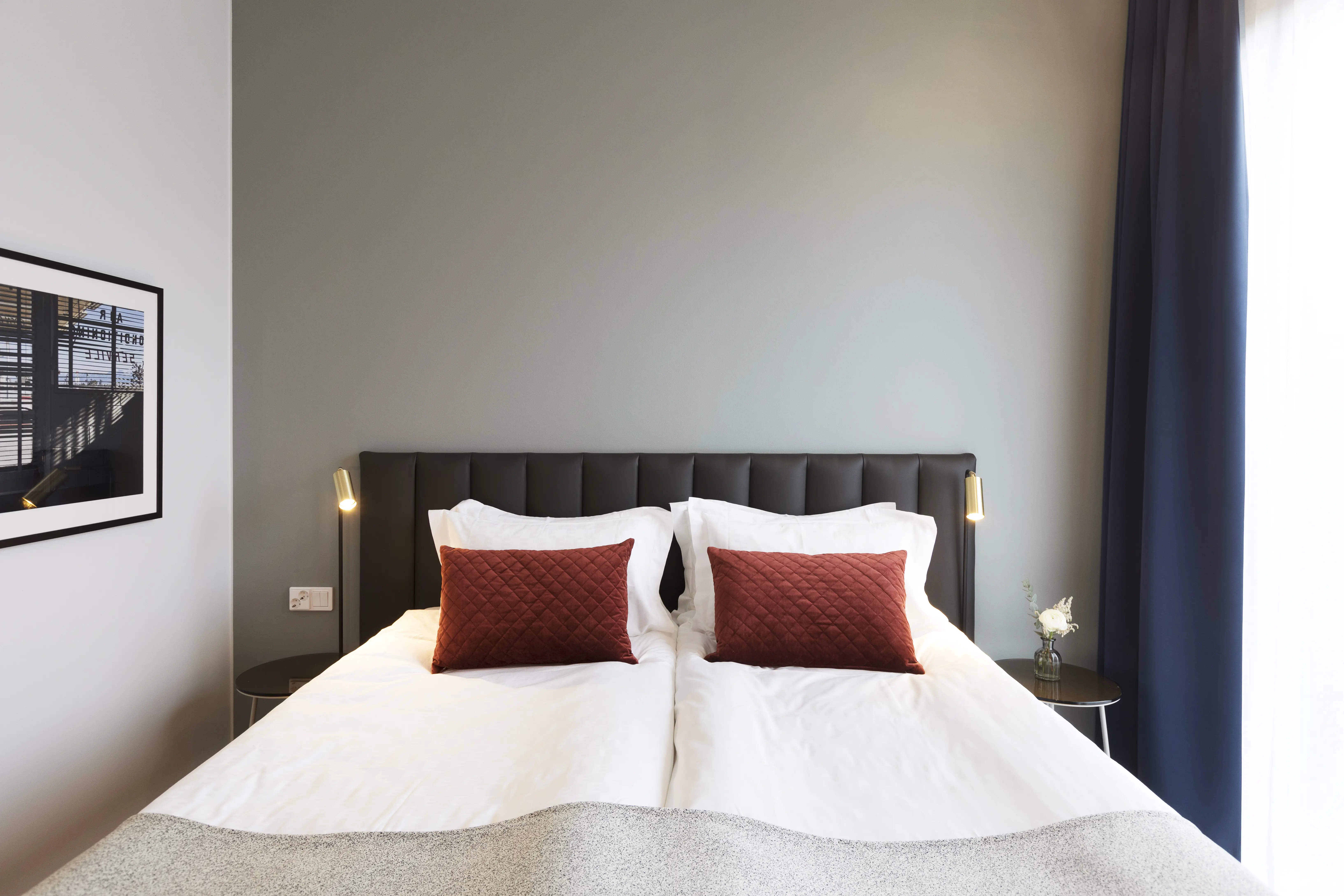 Ljust hotellrum med säng, mörk sänggavel och små sänglampor