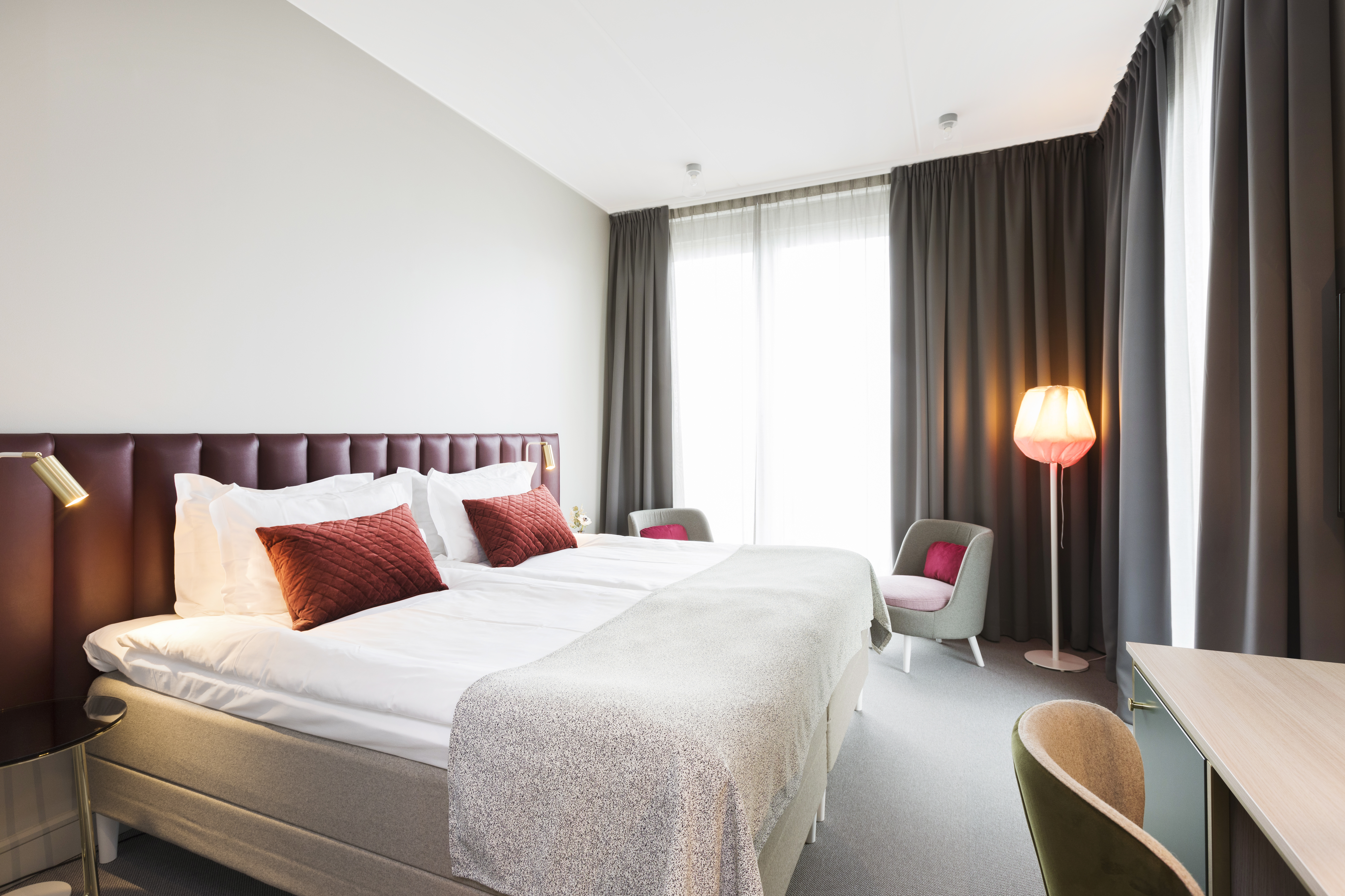 Bright hotel room with bed, burgundy headboard and large window