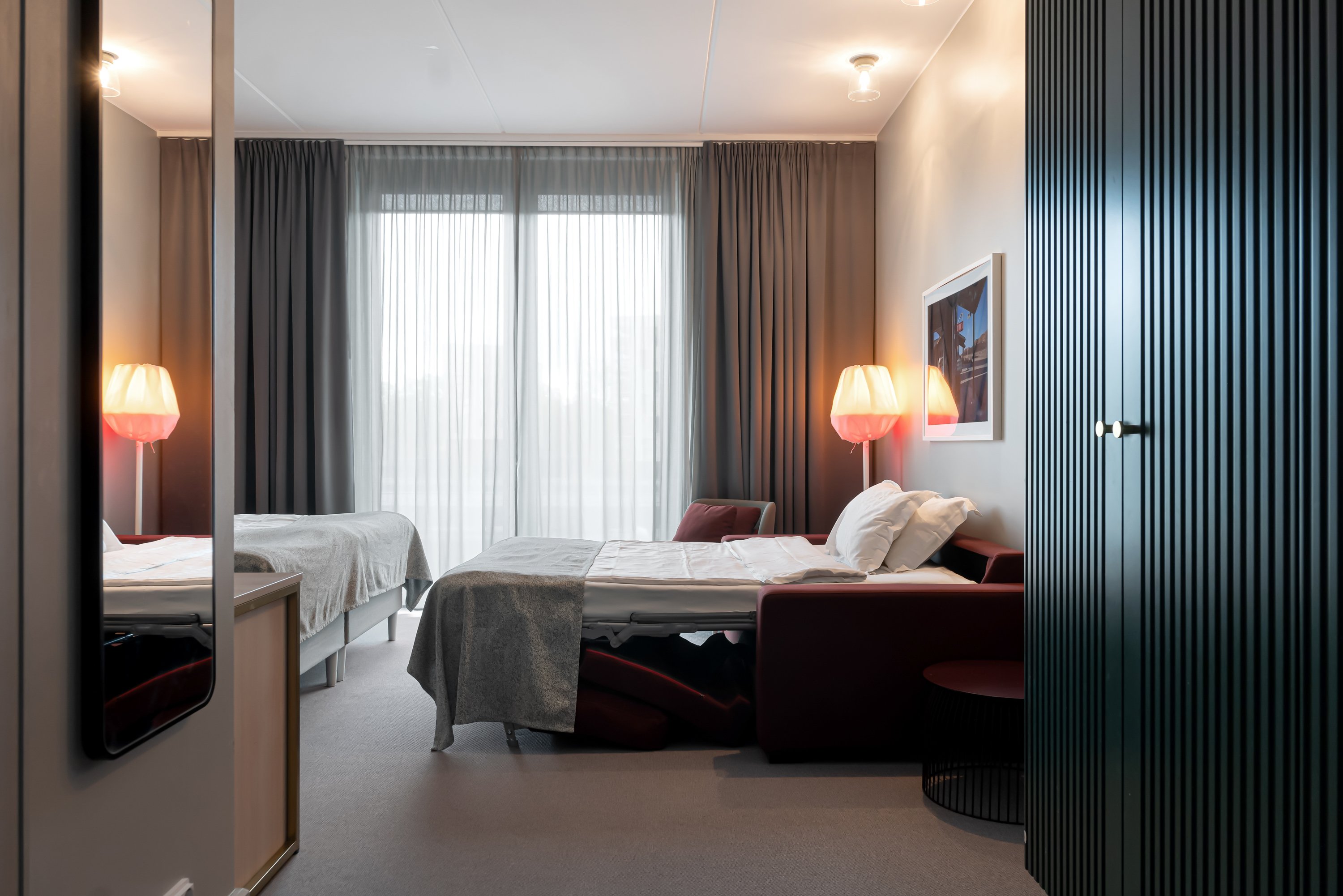 Bright hotel room with wardrobe, sofa bed and large window