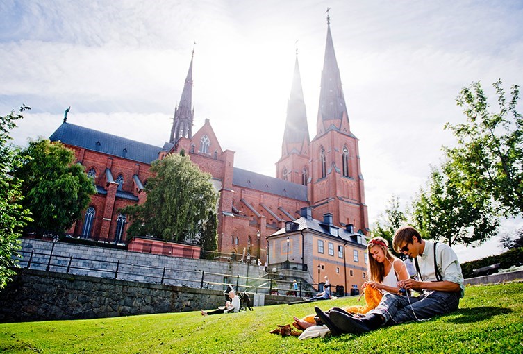 Personer sitter i gräset utanför Uppsala Domkyrka