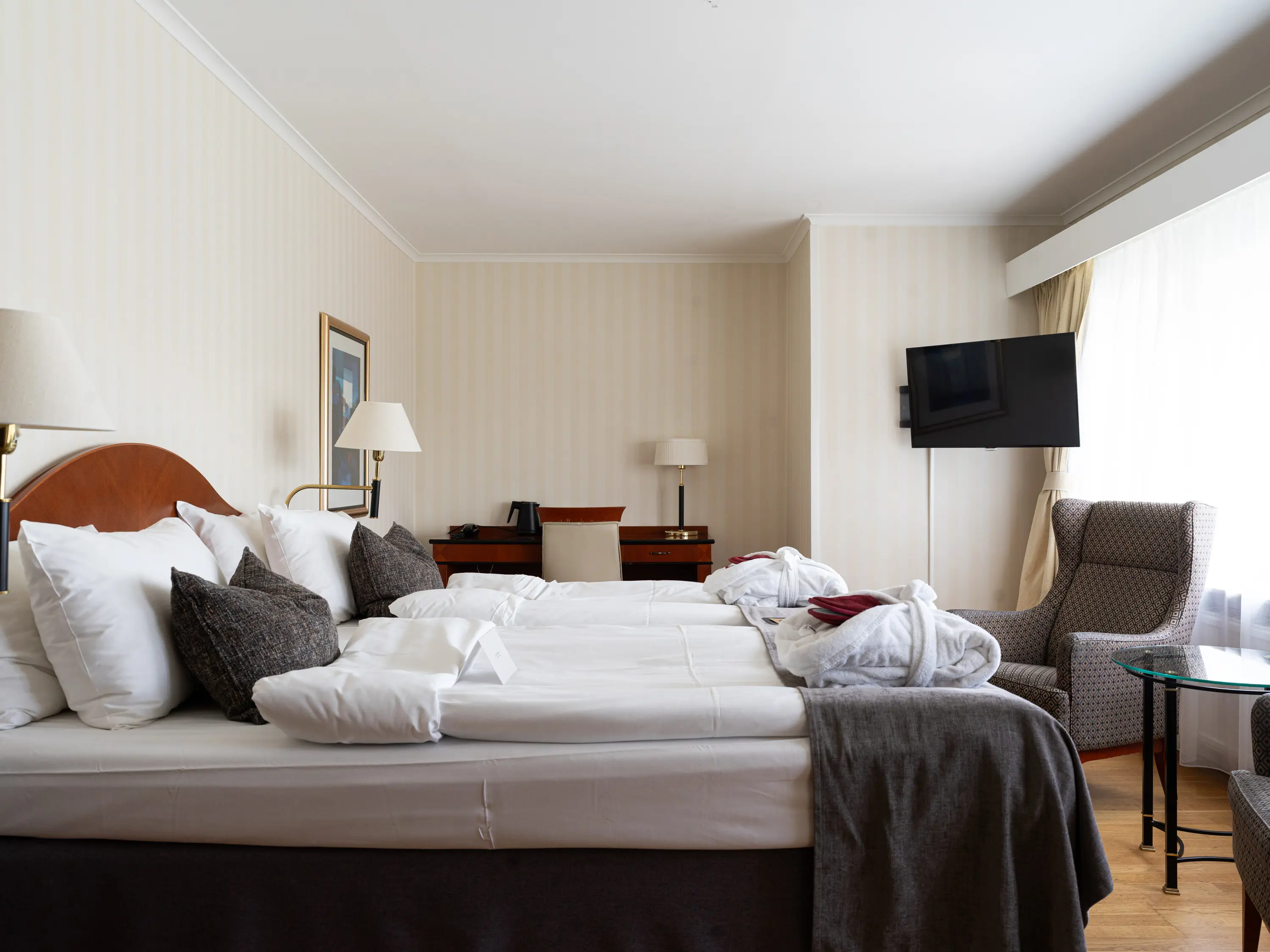 Mysigt hotellrum med morgonrock på säng, garderob och fåtöljer