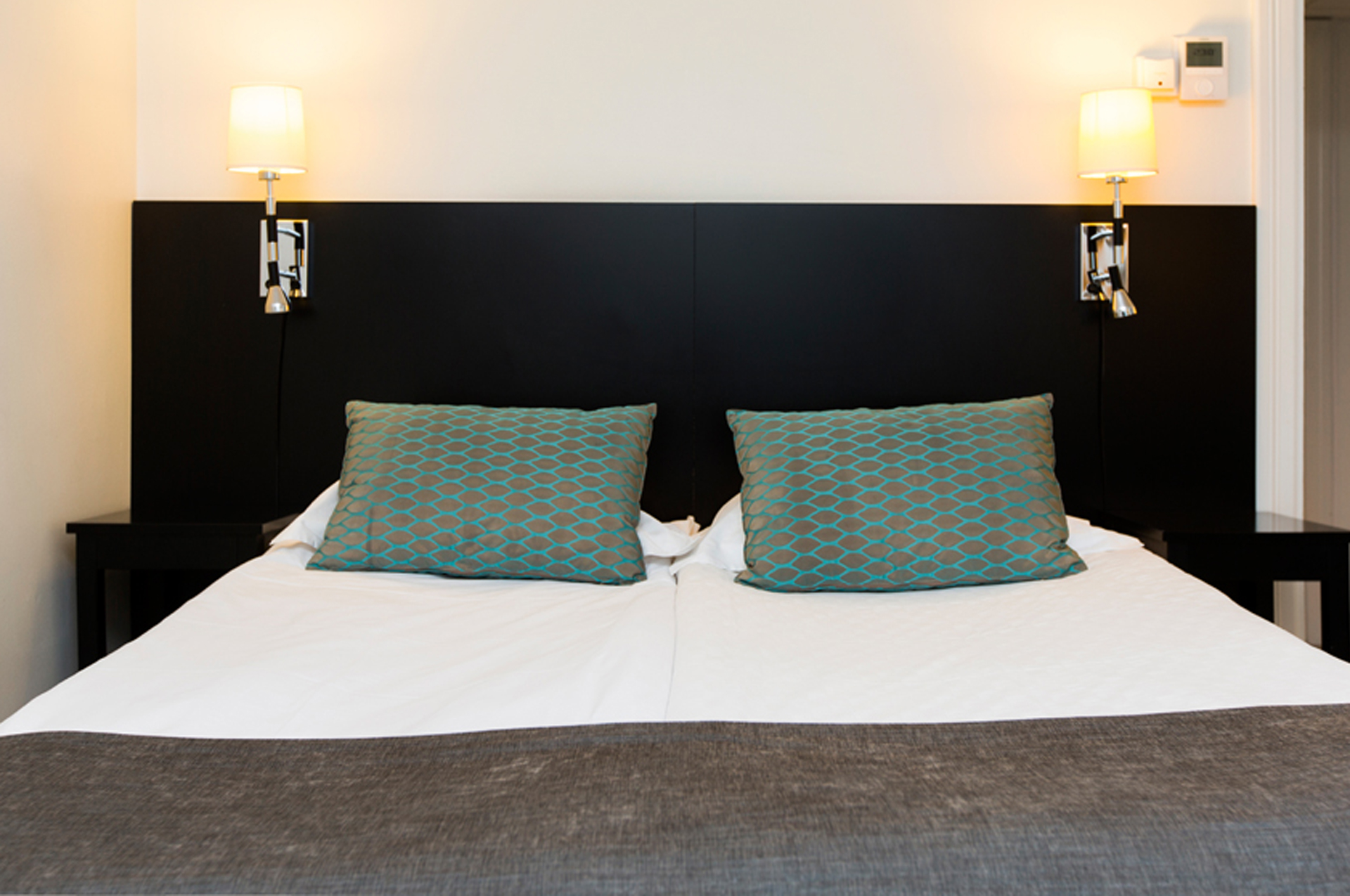 Mysigt hotellrum med säng, svart sänggavel och sänglampor