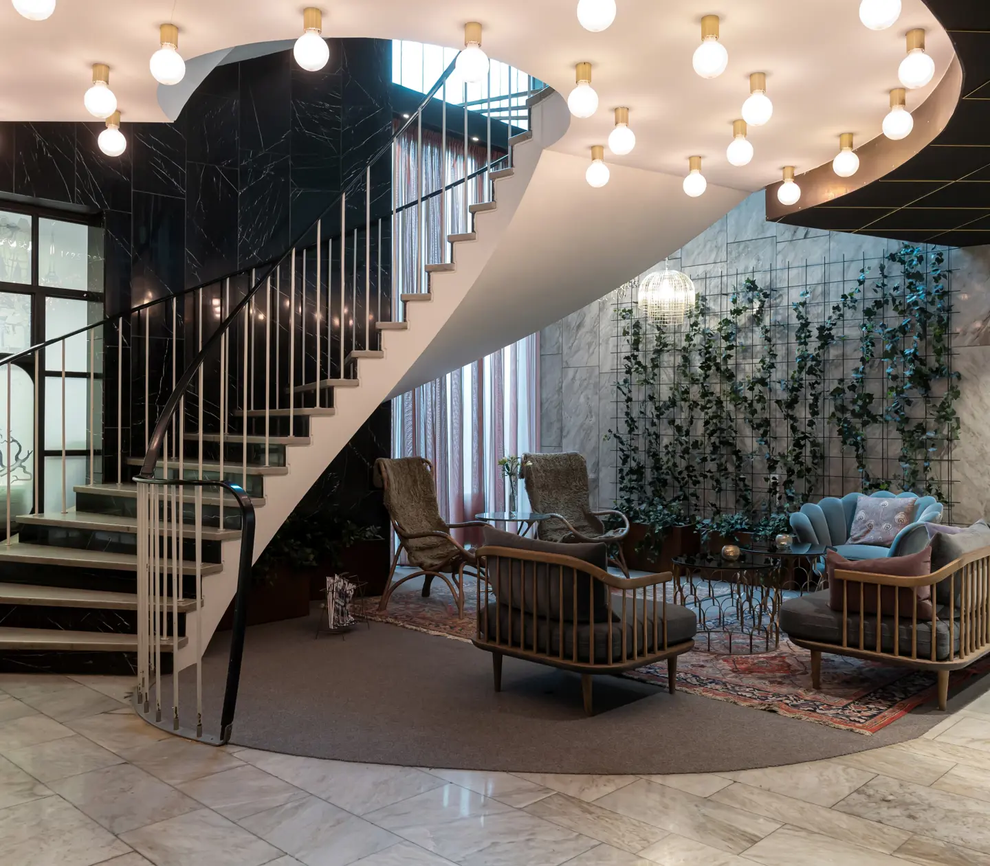 Hotellobby med loungemöbler, växter längs väggarna och trapp med taklampor