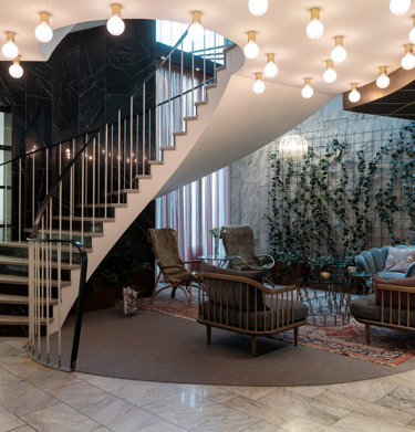 Hotel lobby with lounge furniture, plants along the walls and staircase with ceiling lights