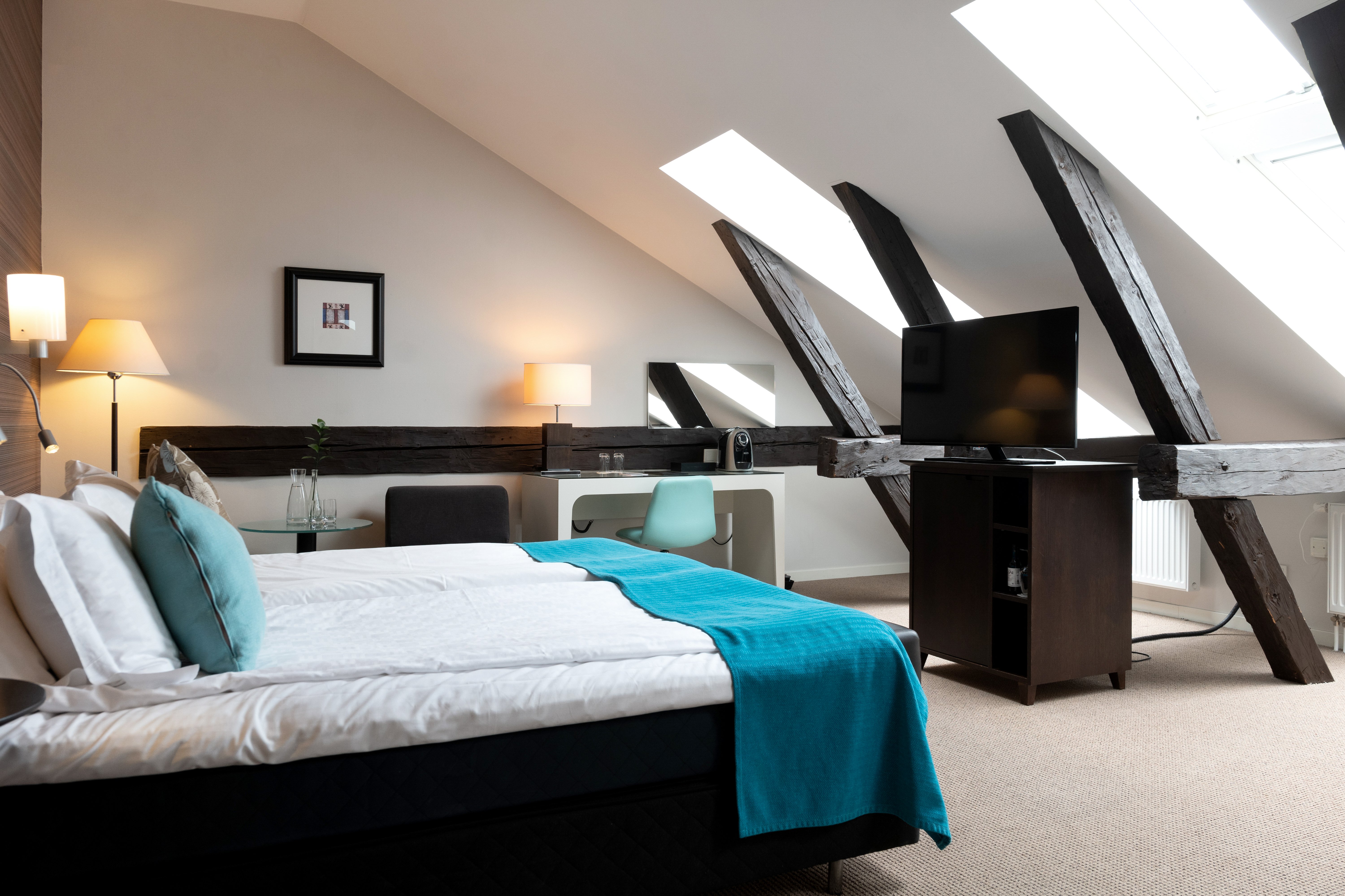 Hotel room with wooden beams, slanted ceiling, double bed and desk