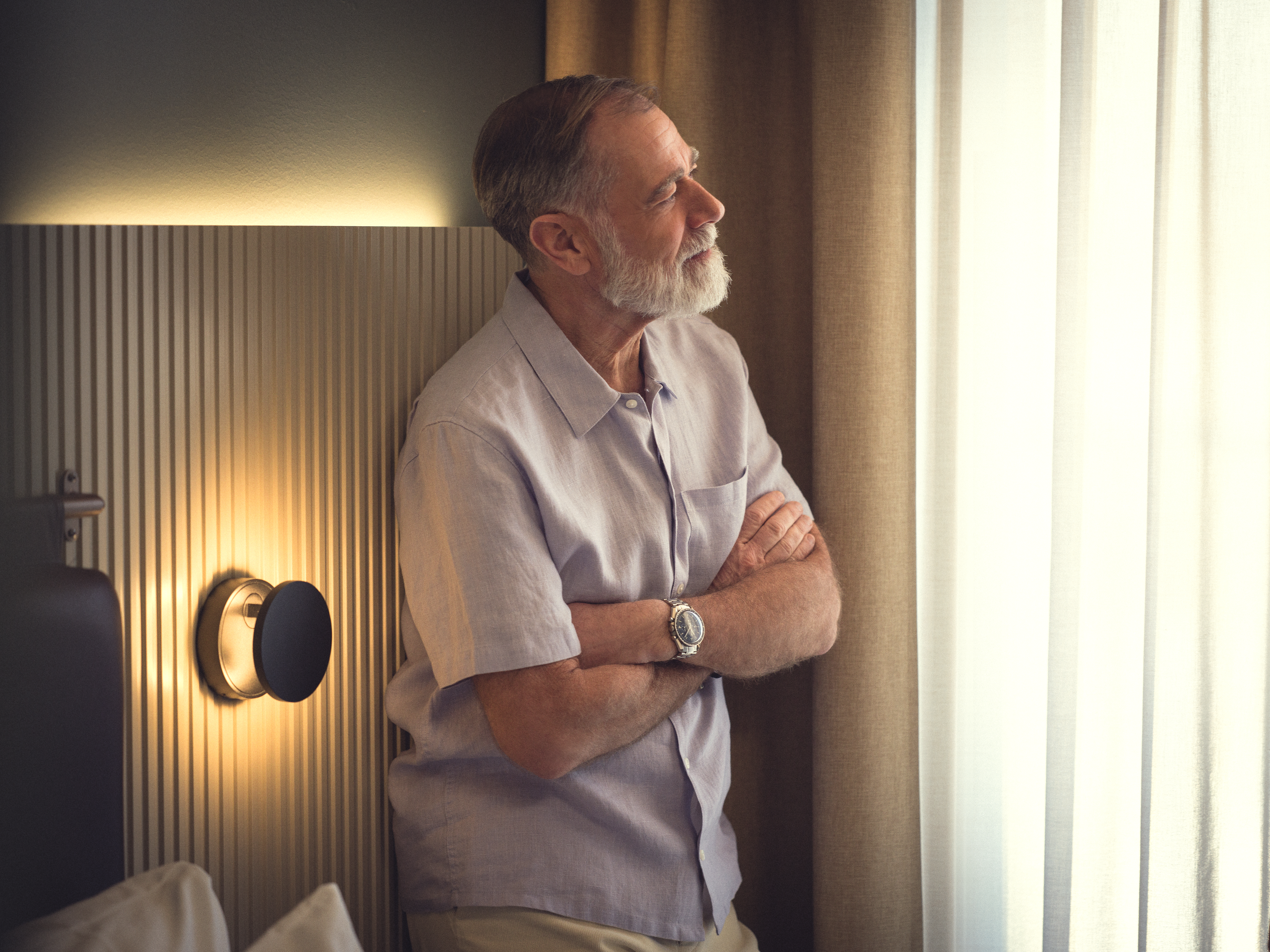 Äldre man kontemplerar medan han ser ut genom fönstret i ett mysigt rum