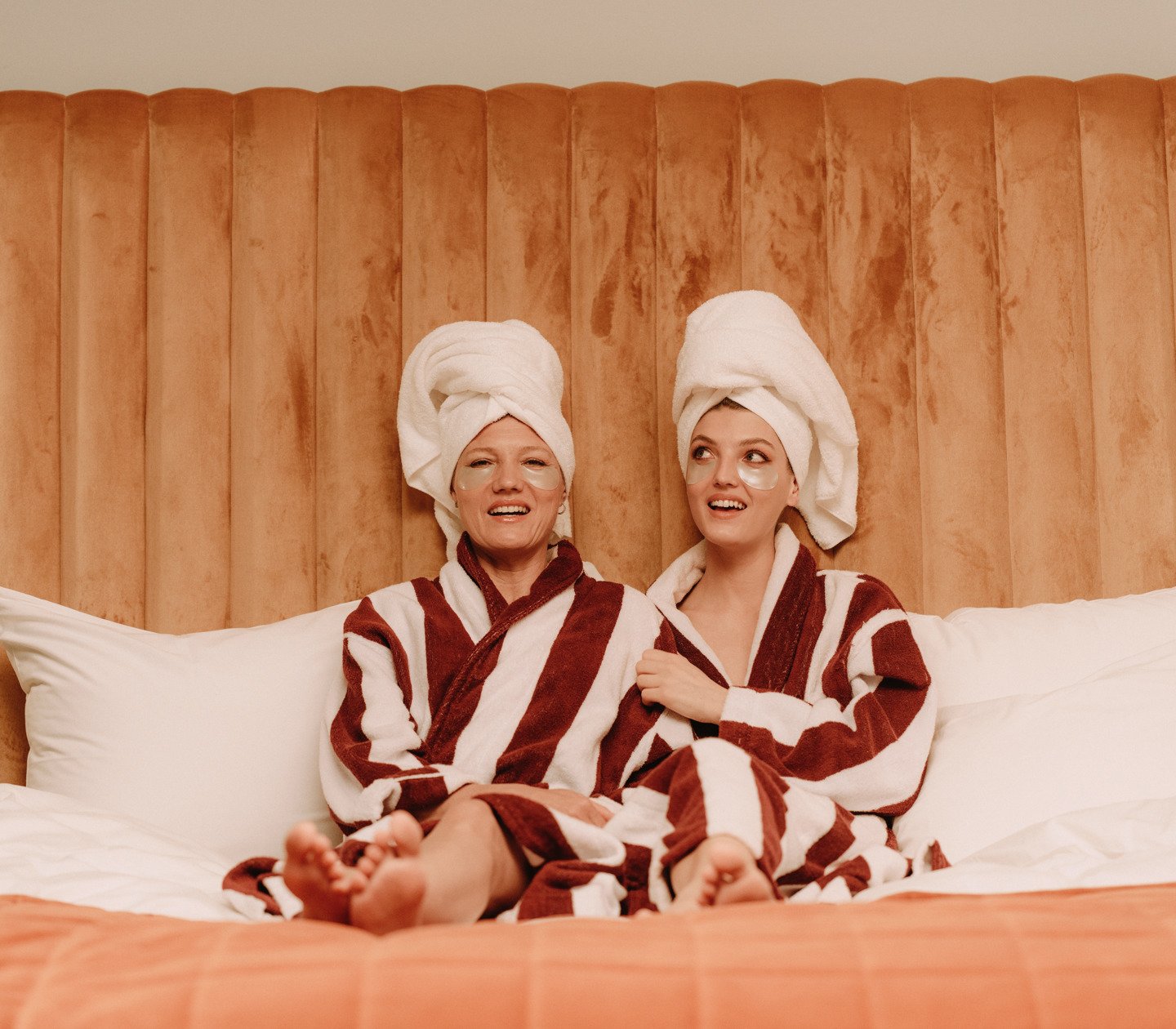 Mother and daughter sitting in bathrobes on hotel bed
