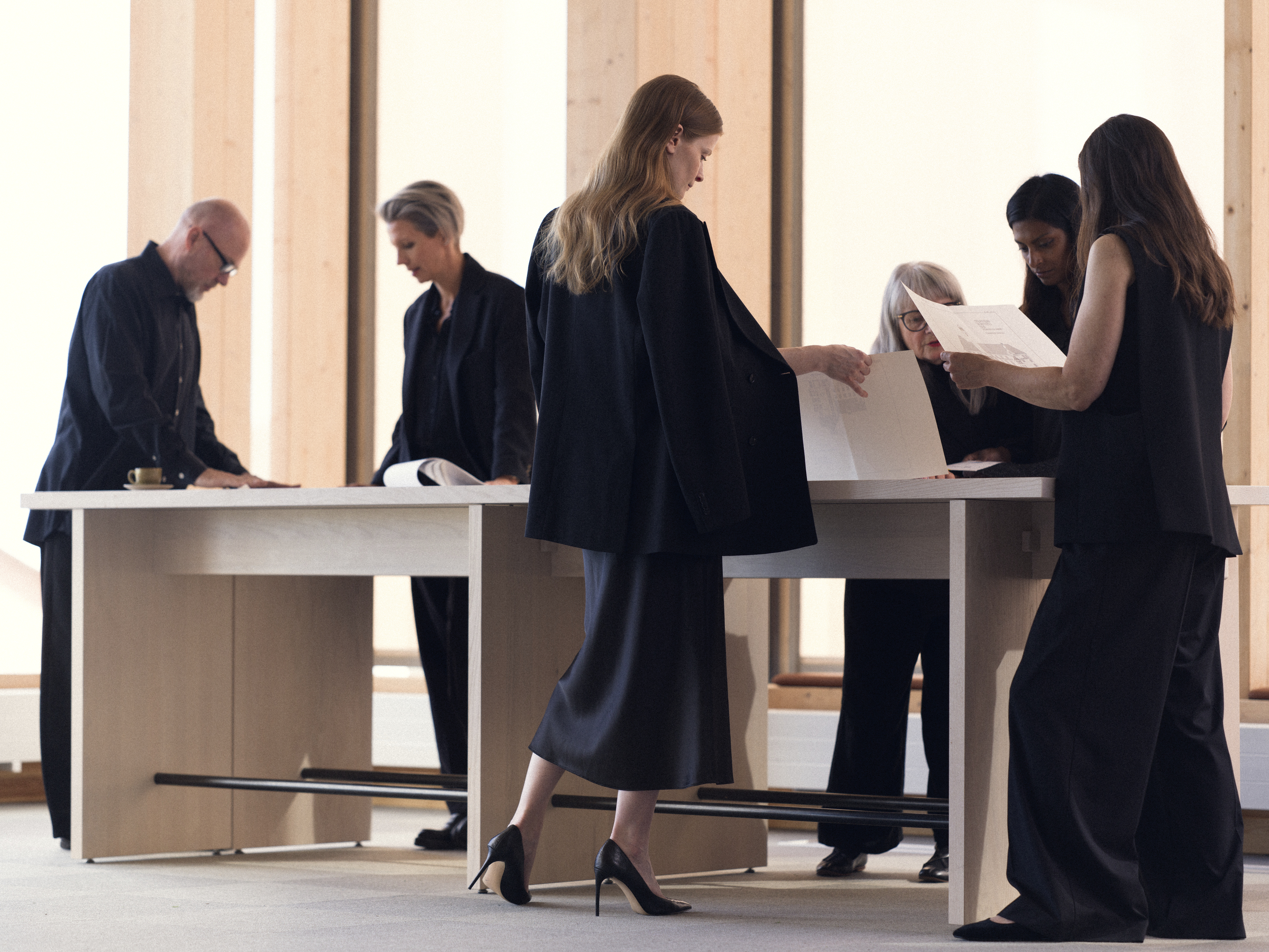 A group of professionals in formal attire reviewing documents around a large table in a modern office setting.
