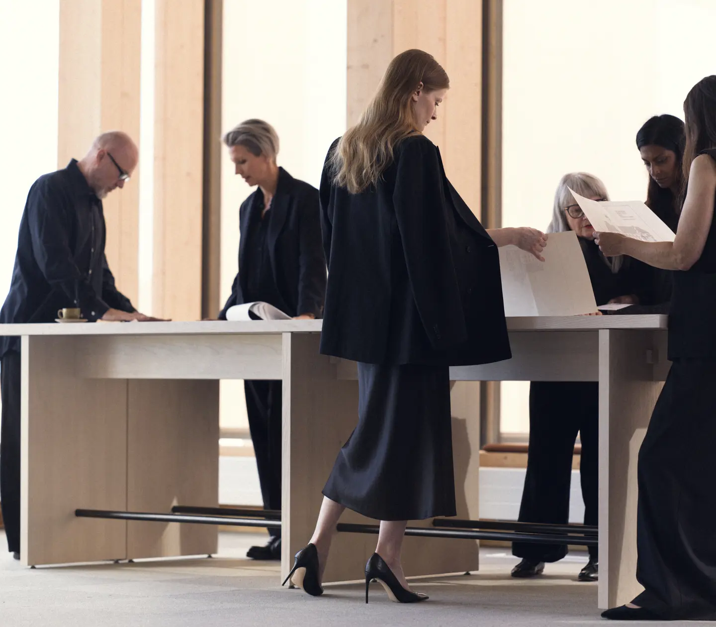 A group of professionals in formal attire reviewing documents around a large table in a modern office setting.