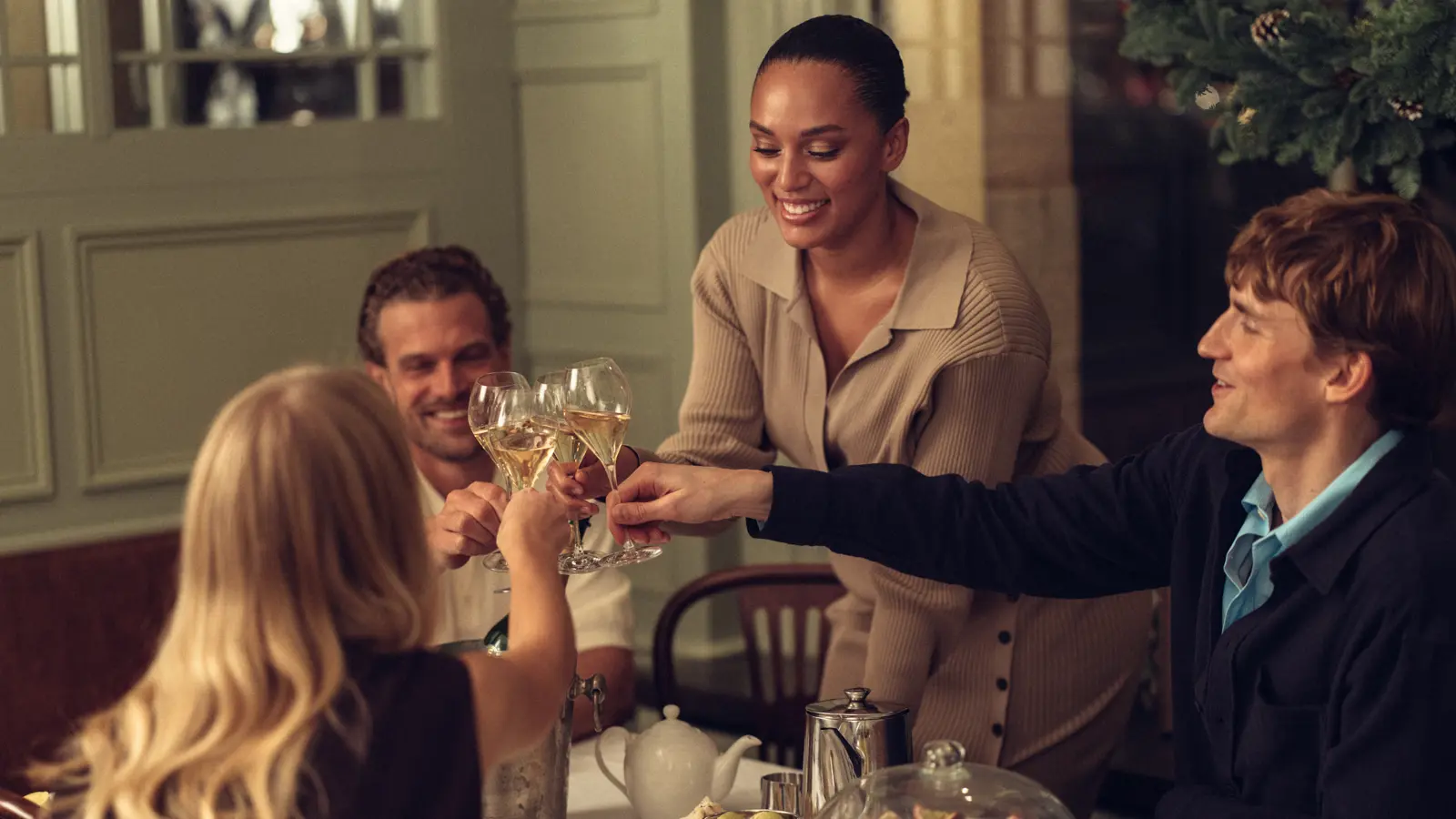 Fyra personer skålar med vinglas runt ett bord fyllt med te och desserter i en restaurangmiljö