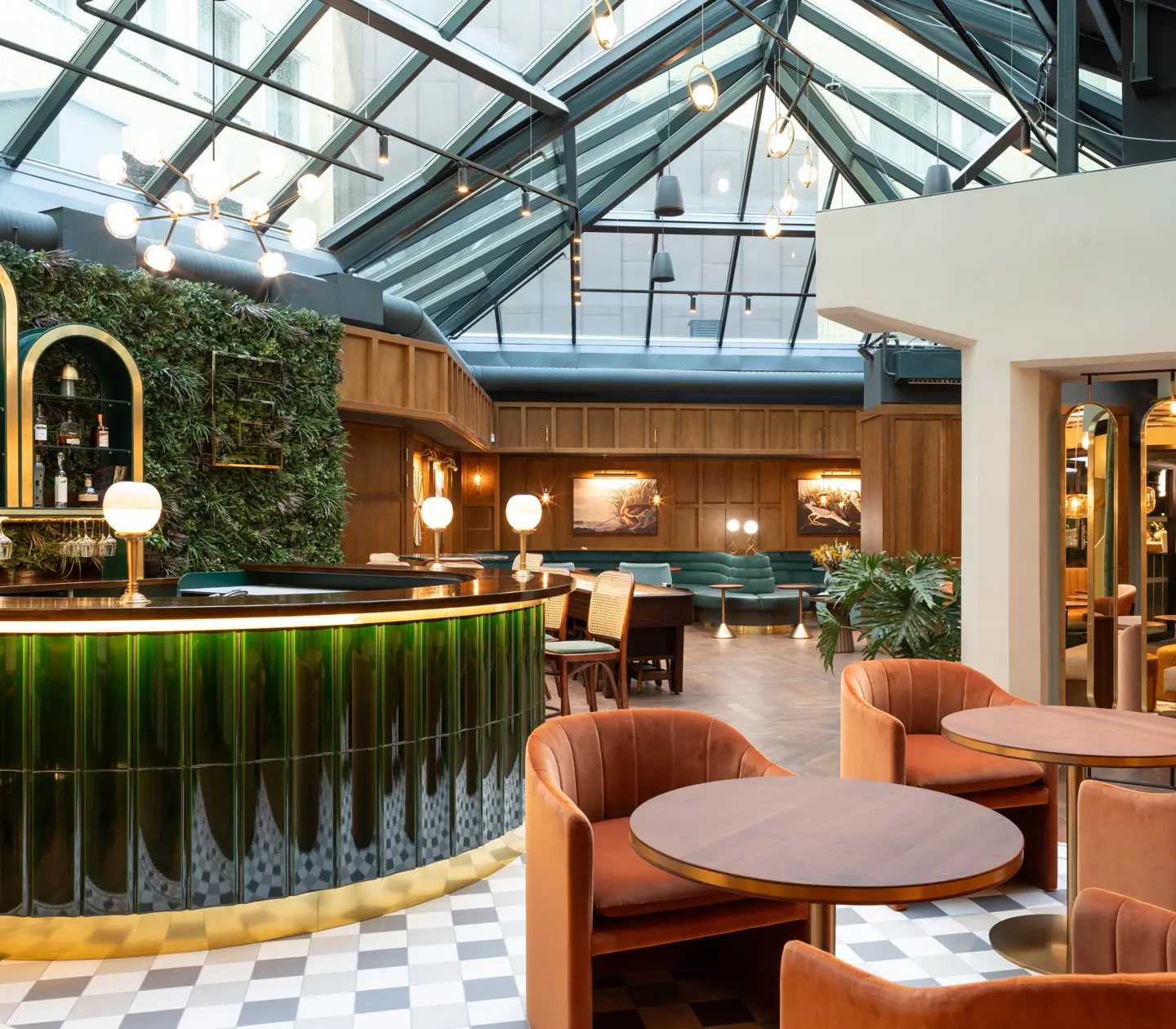 Modern interiör av en lounge med glasat tak, eleganta gröna och bruna möbler, samt en stilfull bar i grönt glas