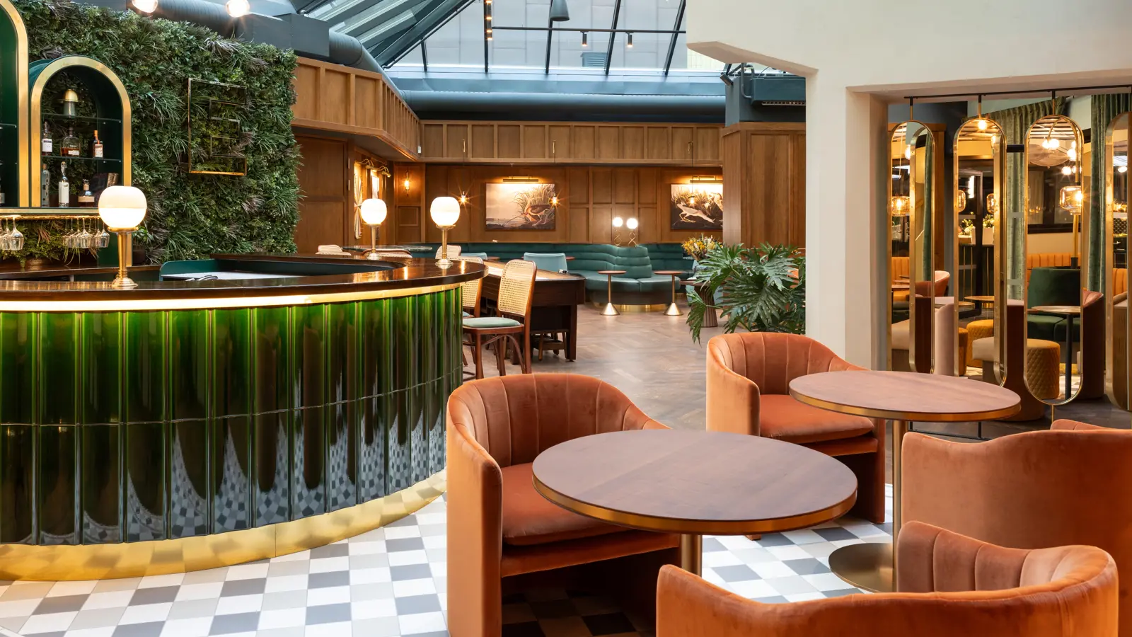 Modern interiör av en lounge med glasat tak, eleganta gröna och bruna möbler, samt en stilfull bar i grönt glas