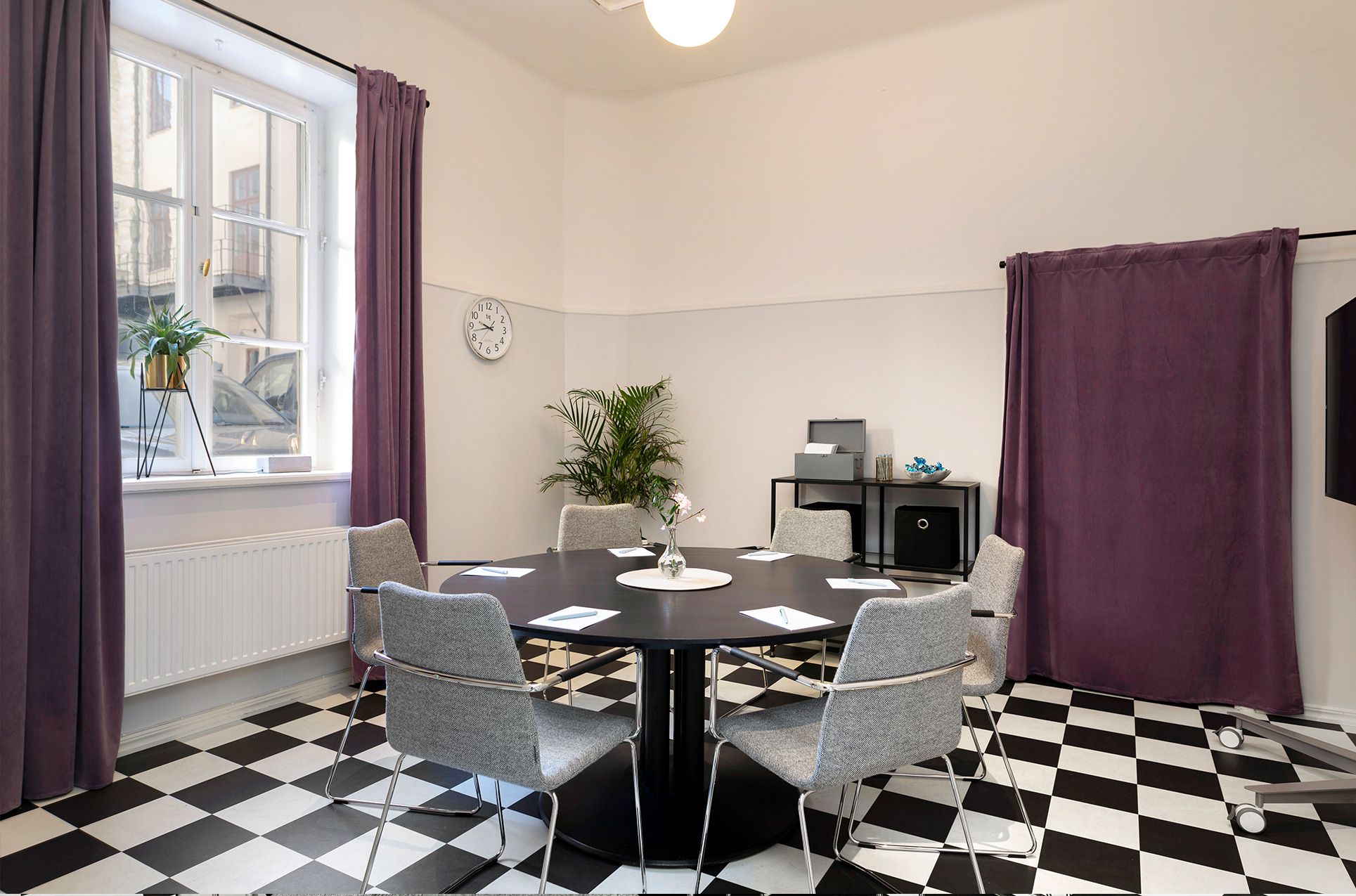 Konferensrum med schackrutigt golv, runt bord och stort fönster