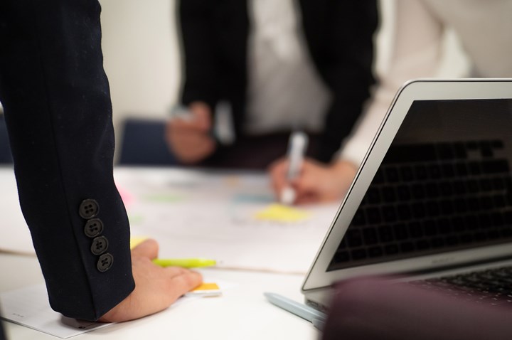 Personer som lutar sig över konferensbord med pennor i händerna