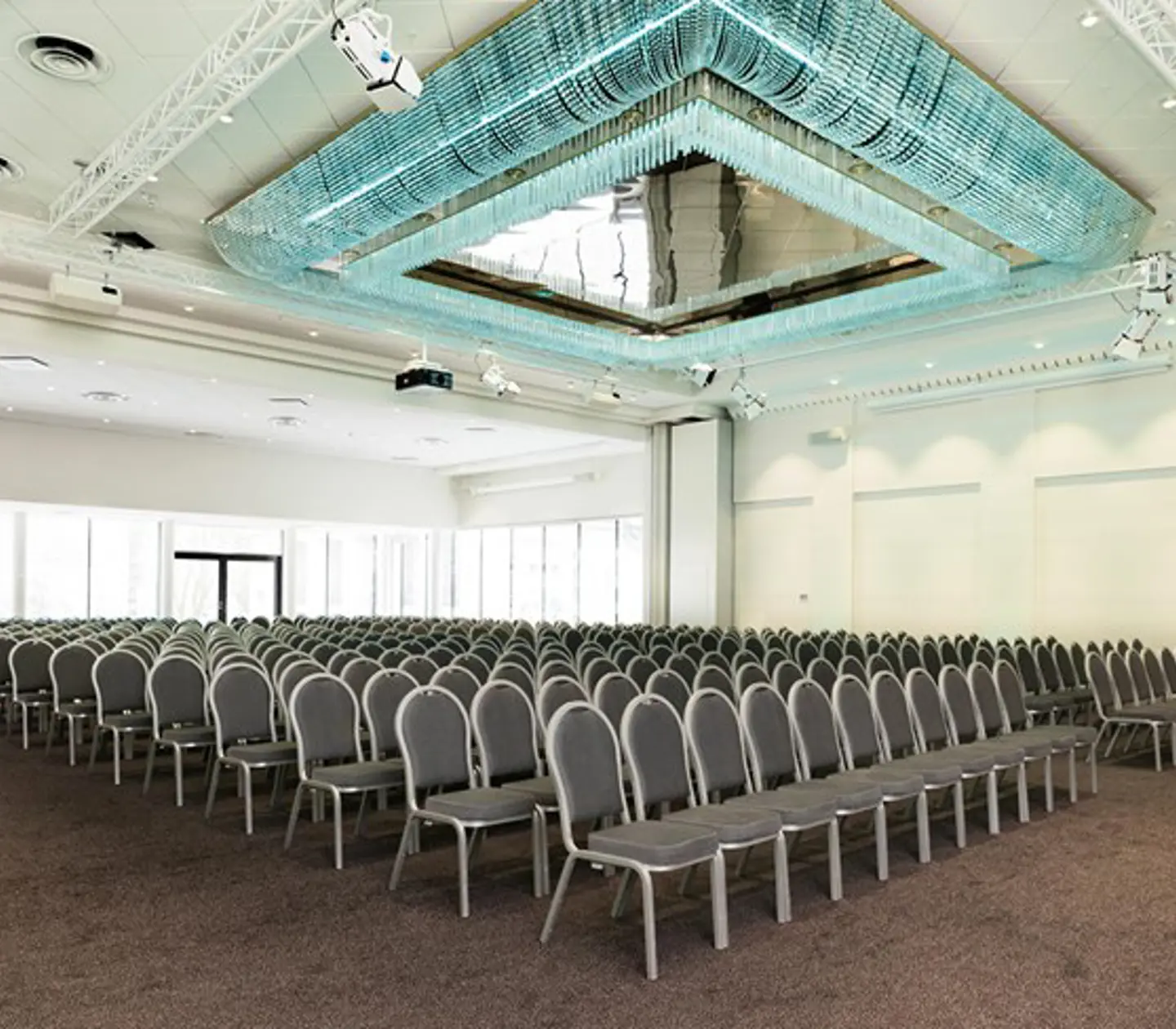 Många stolar i biosittning i konferensrum med blå fyrkantig lampa