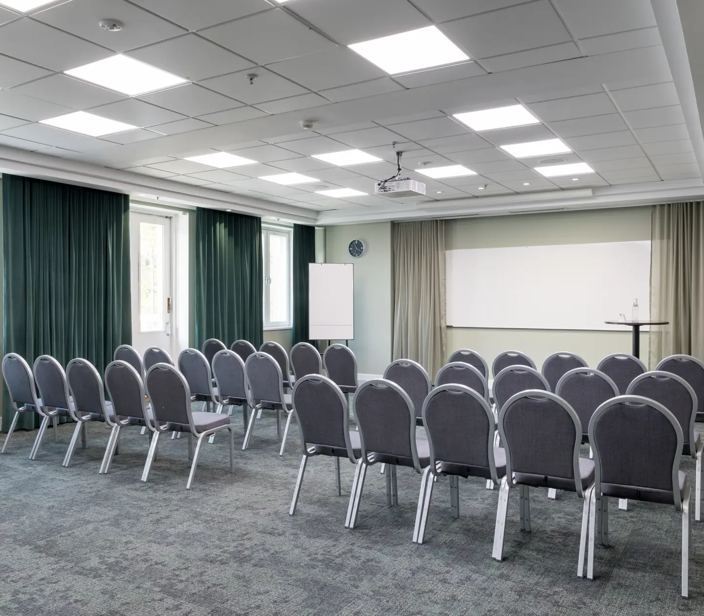 Ljust konferensrum med stolar i rader, fönster och whiteboard