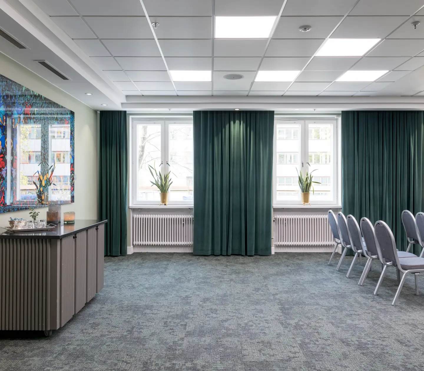 Ljust konferensrum med stolar i rader, fönster och färgglad tavla