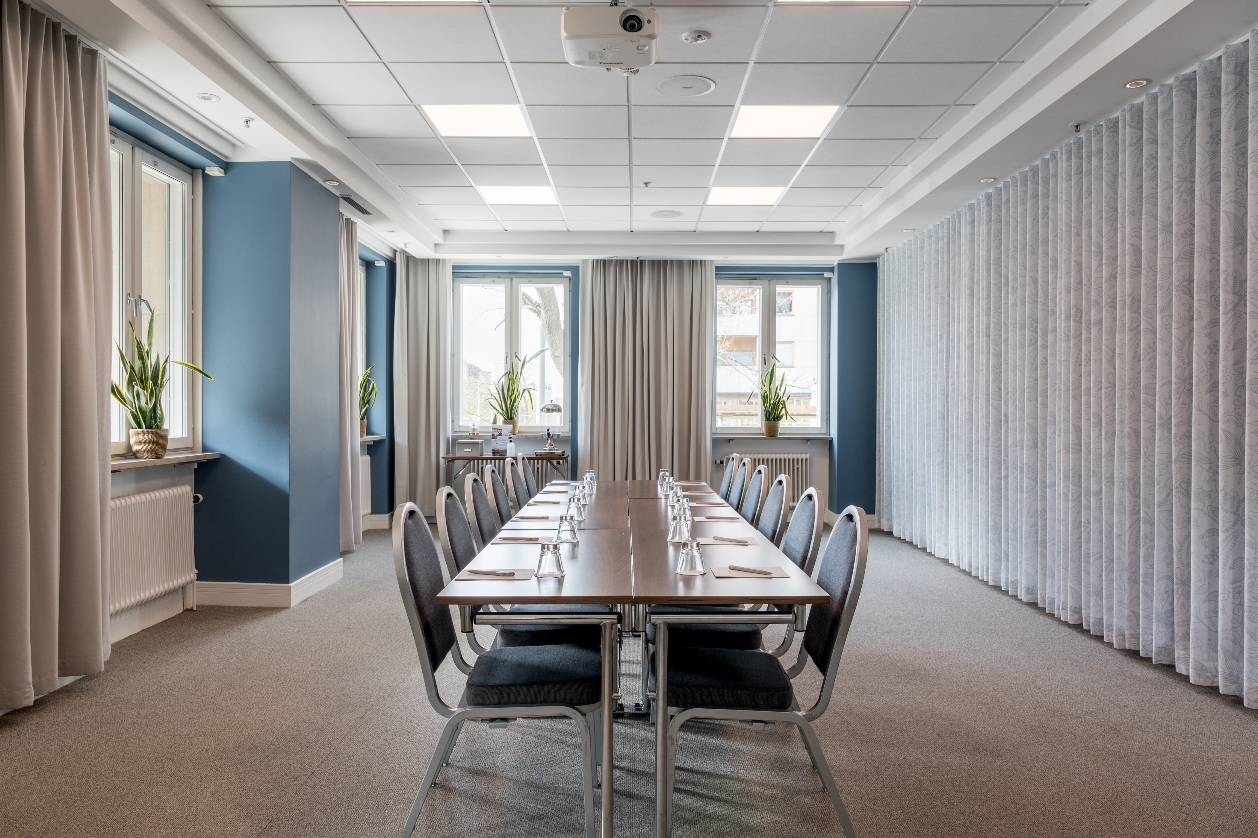 Bright conference room with a large table, chairs, curtains, and windows.