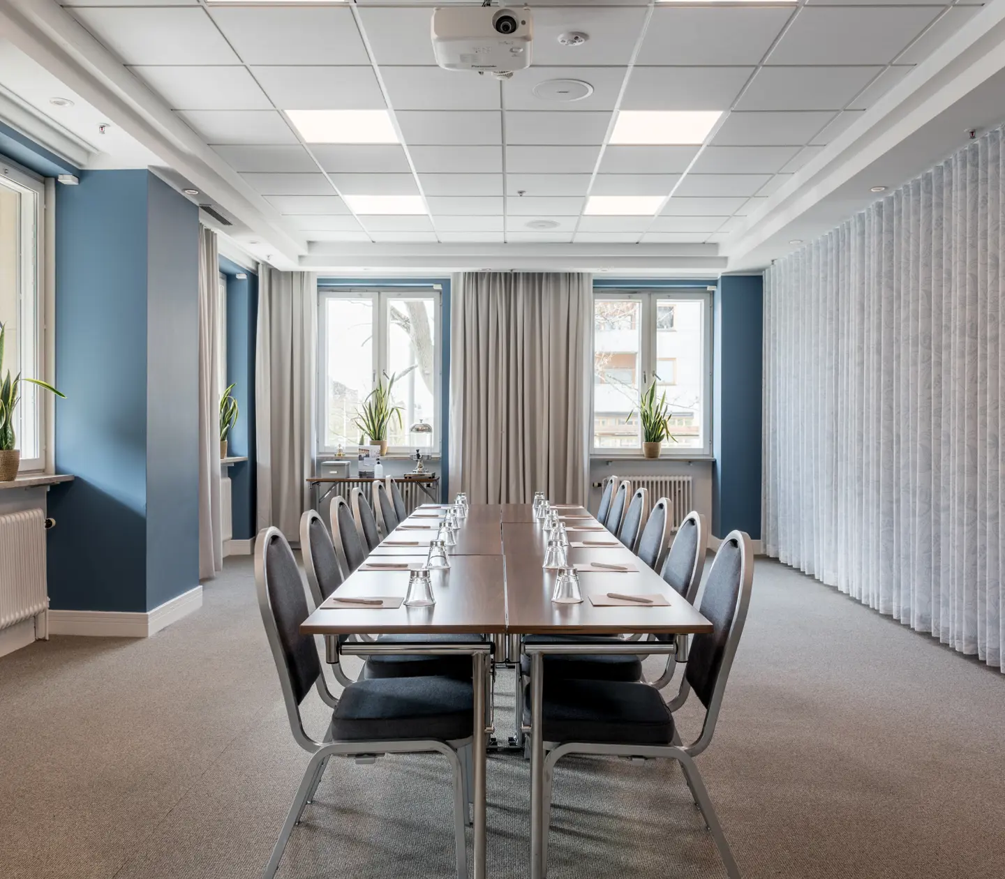 Ljust konferensrum med stort bord, stolar, gardiner och fönster