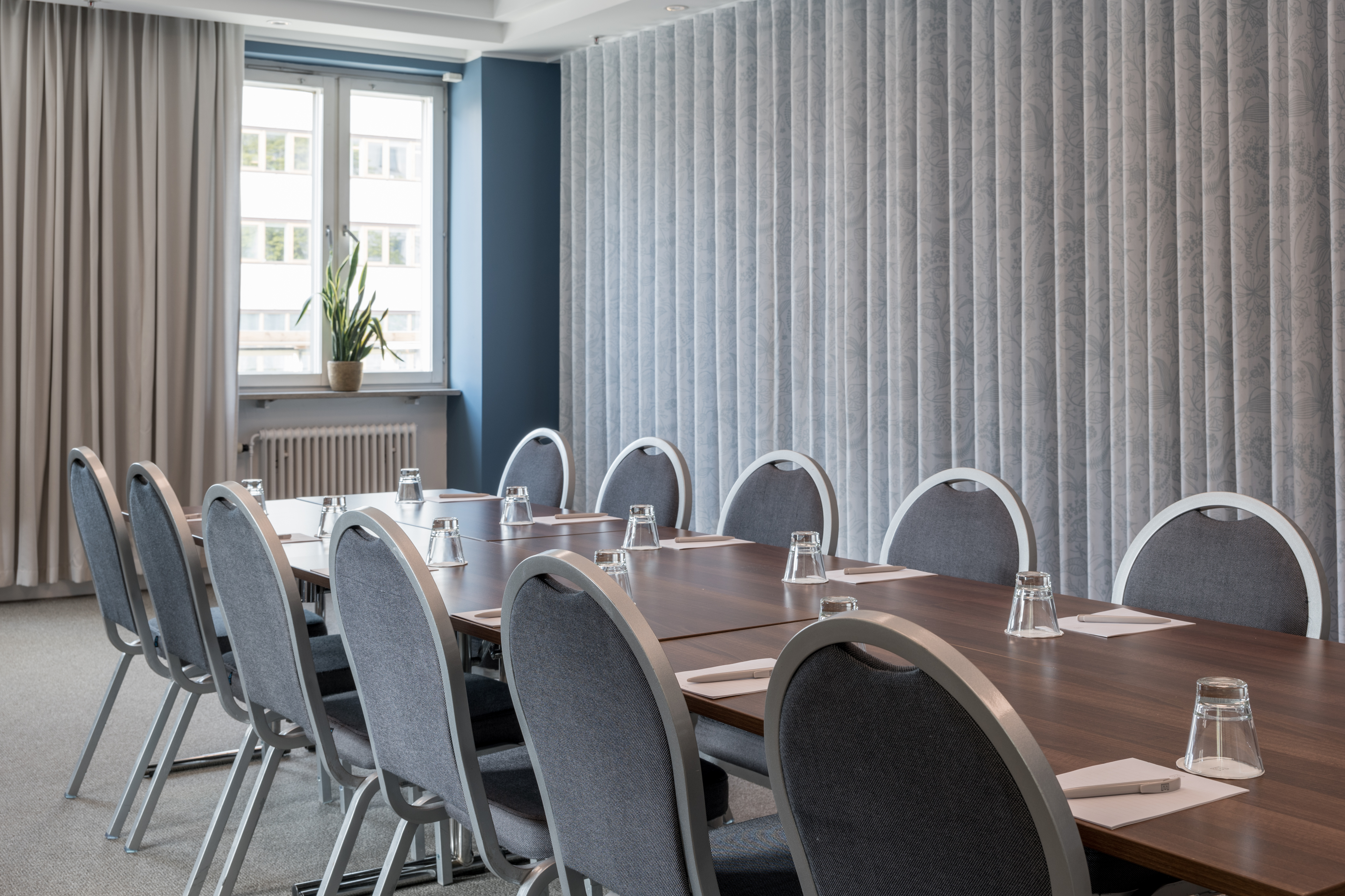 Bright conference room with a large table, chairs, curtains, and windows.