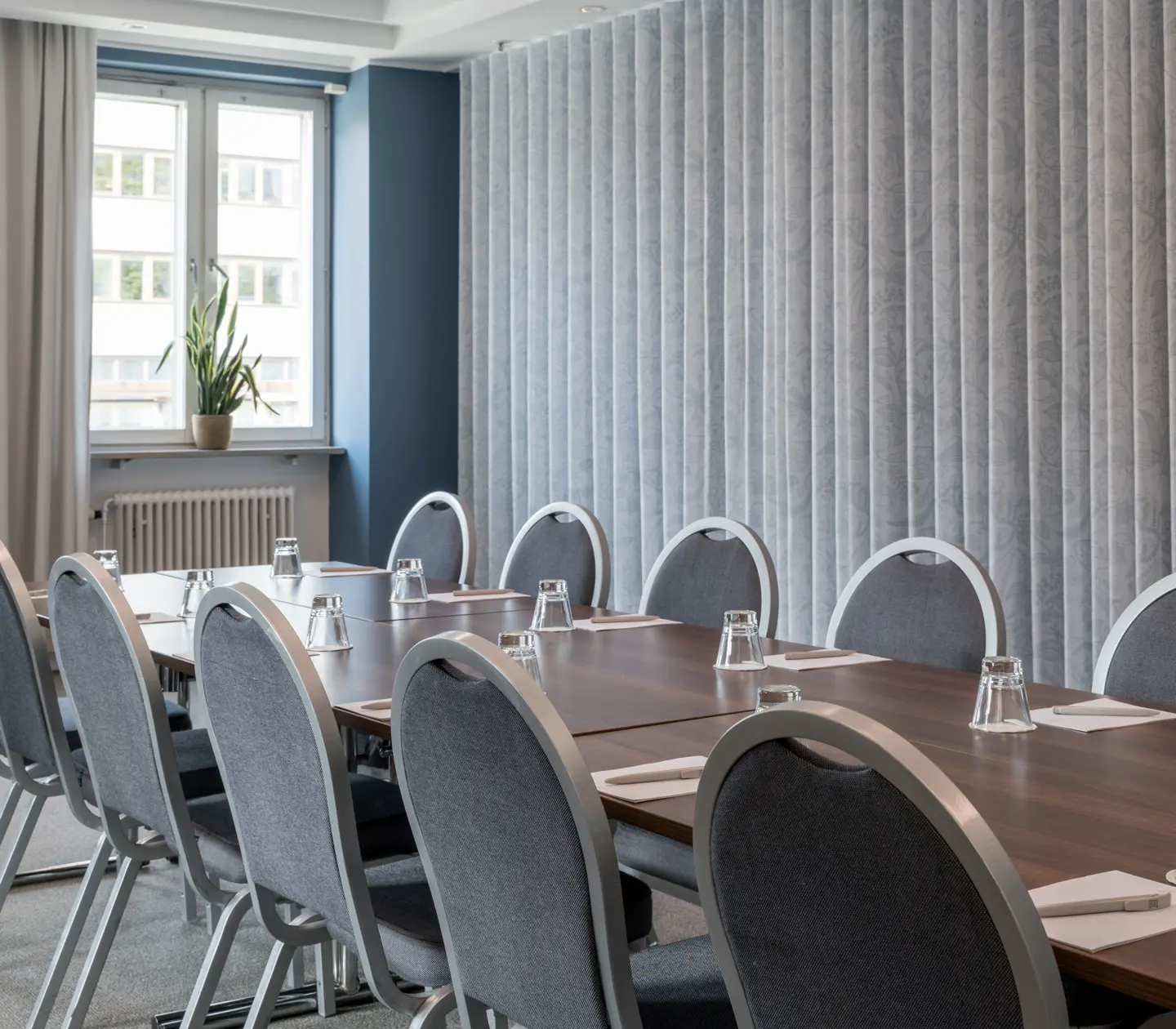 Ljust konferensrum med stort bord, stolar, gardiner och fönster