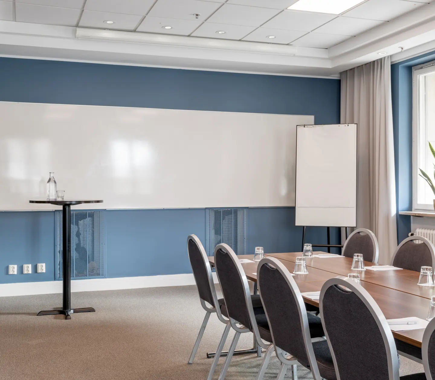 Ljust konferensrum med stort bord, stolar, whiteboard och fönster