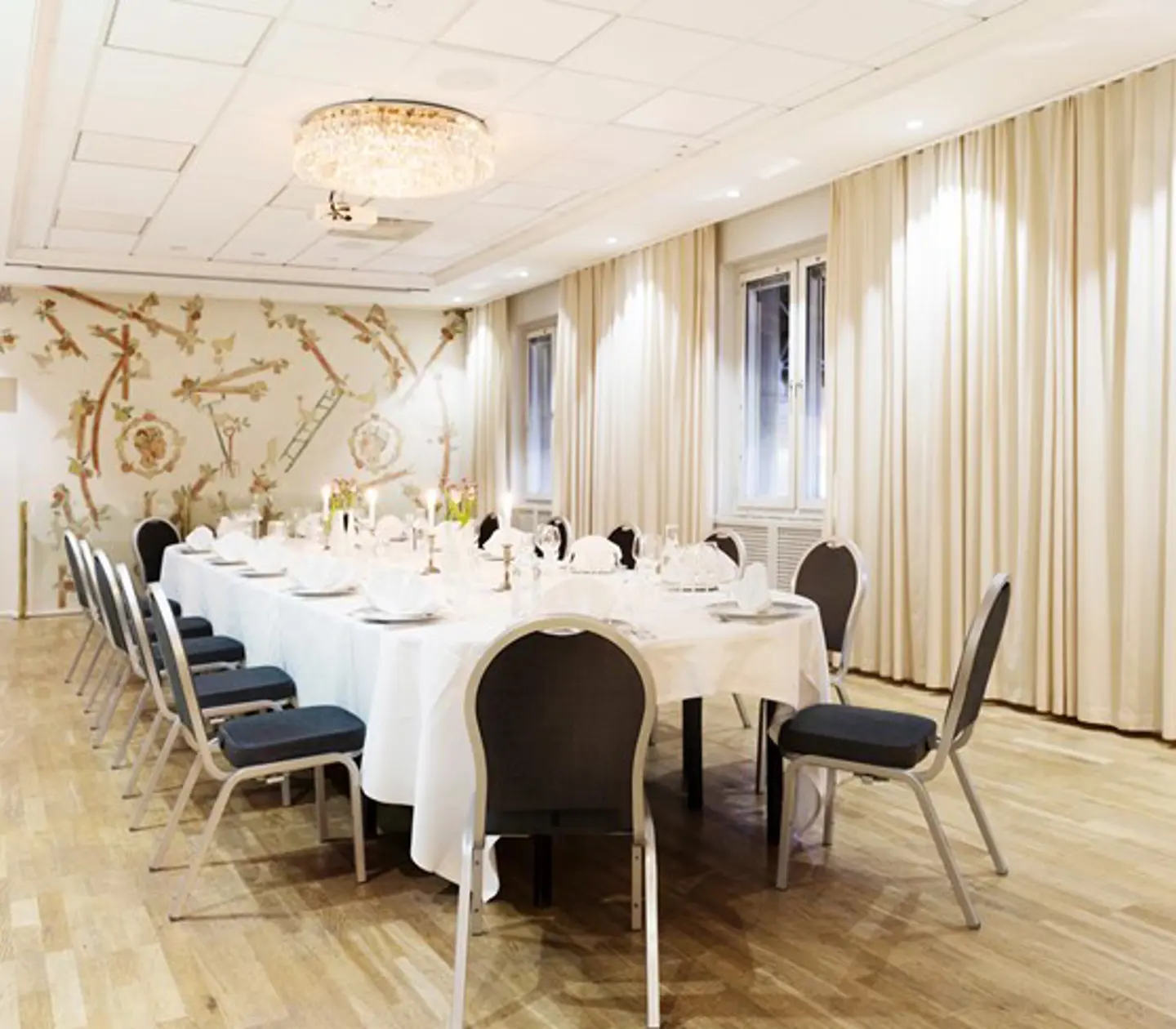 Långt dukat bord i sal med vita gardiner och kristalkronor