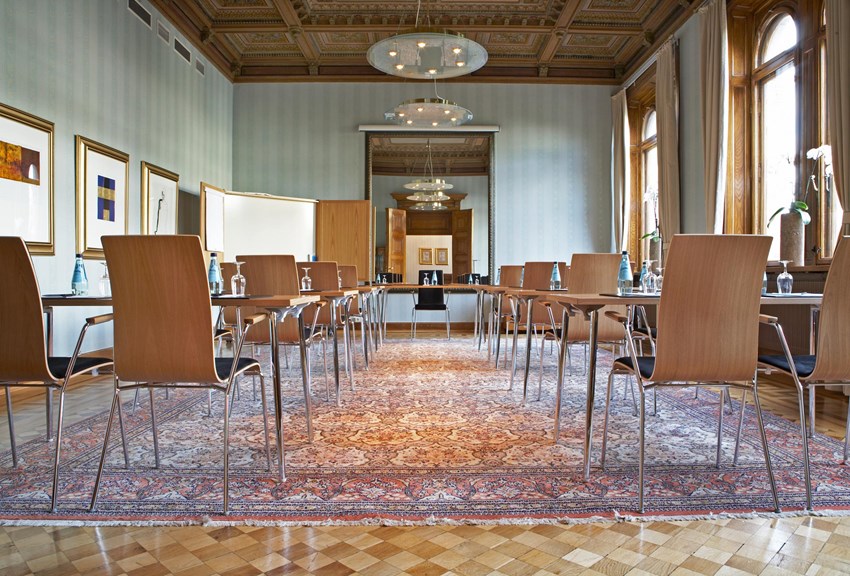 Många stolar i rum med struckaturtak och orientalmatta