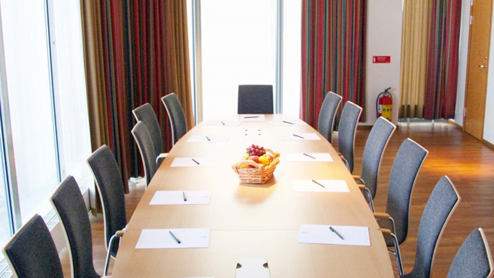 Conference room with board seating, wooden tables, large windows and colorful curtains