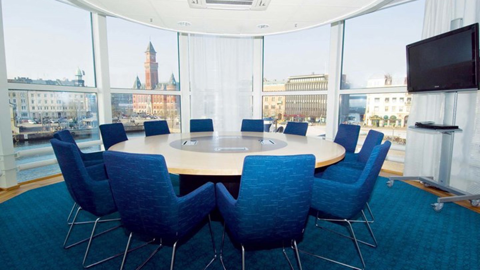 Conference room with round table, blue armchairs, blue carpet and large windows with a view