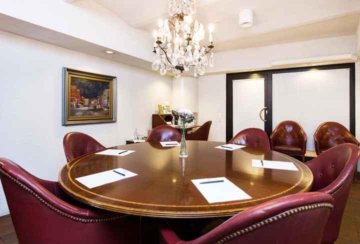 Conference room with round wooden table, red armchairs and white walls