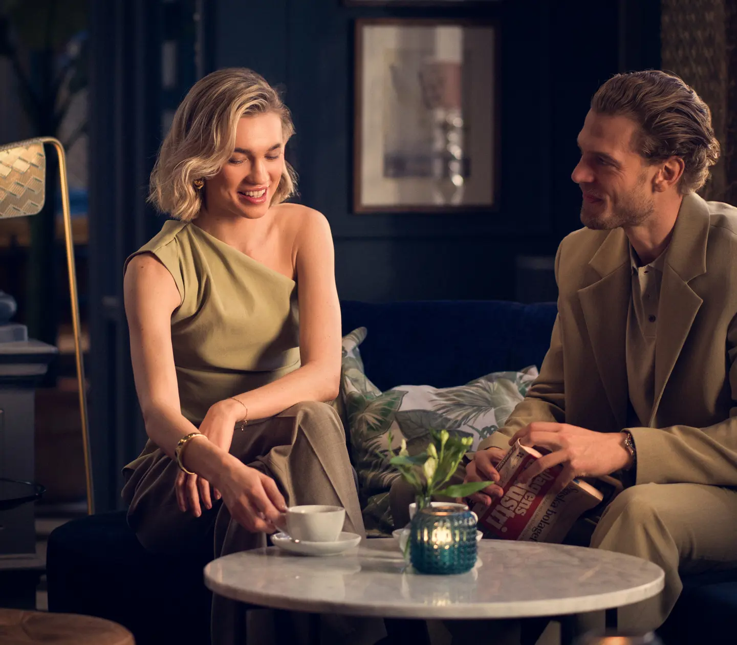 A woman and a man sitting in an elegant hotel lobby with classical details and a checkerboard floor in Helsingborg, Sweden.