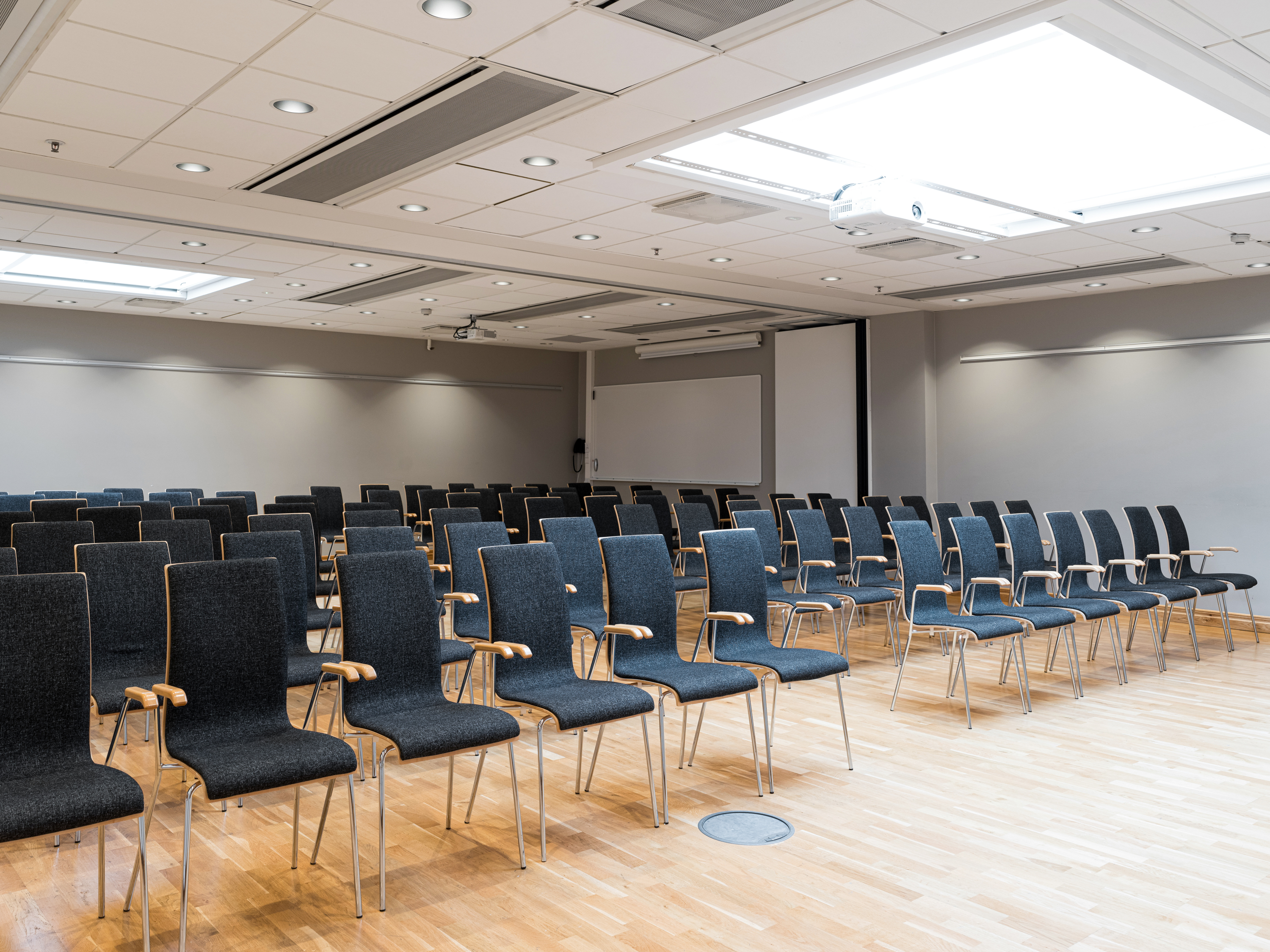 Empty conference room with rows of gray chairs arranged on a wooden floor.