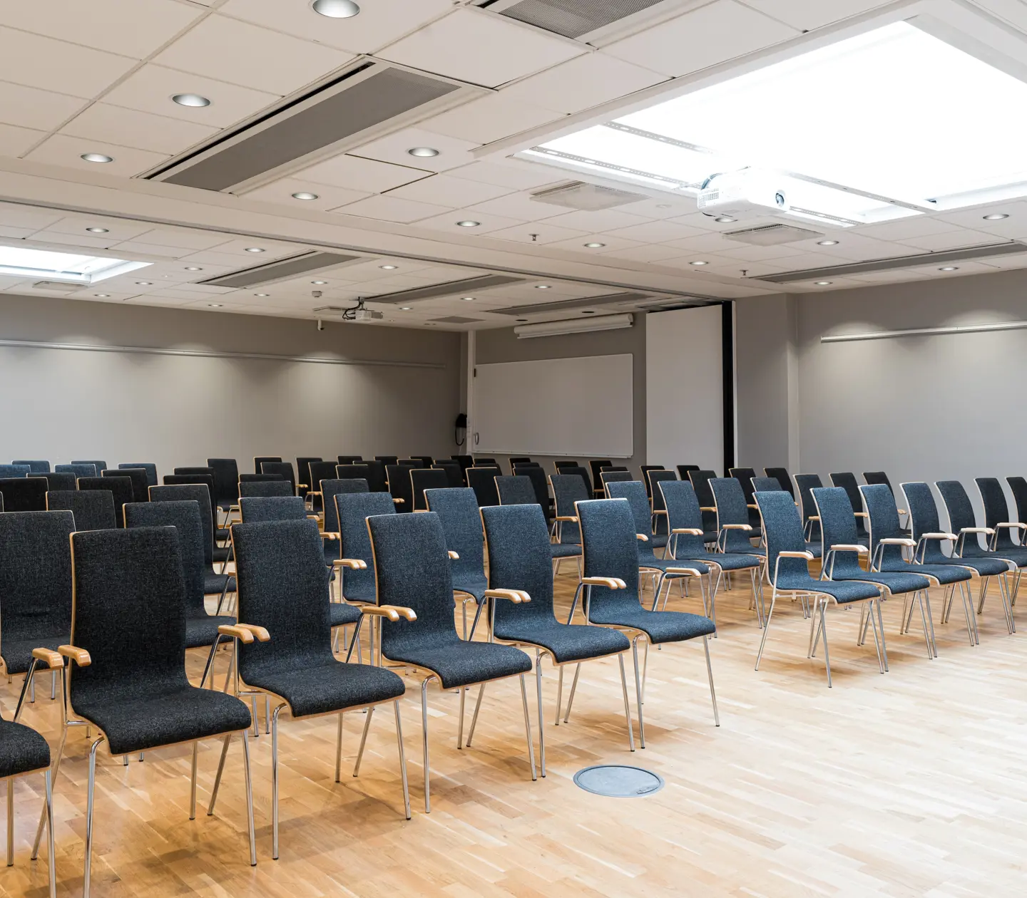 Empty conference room with rows of gray chairs arranged on a wooden floor.