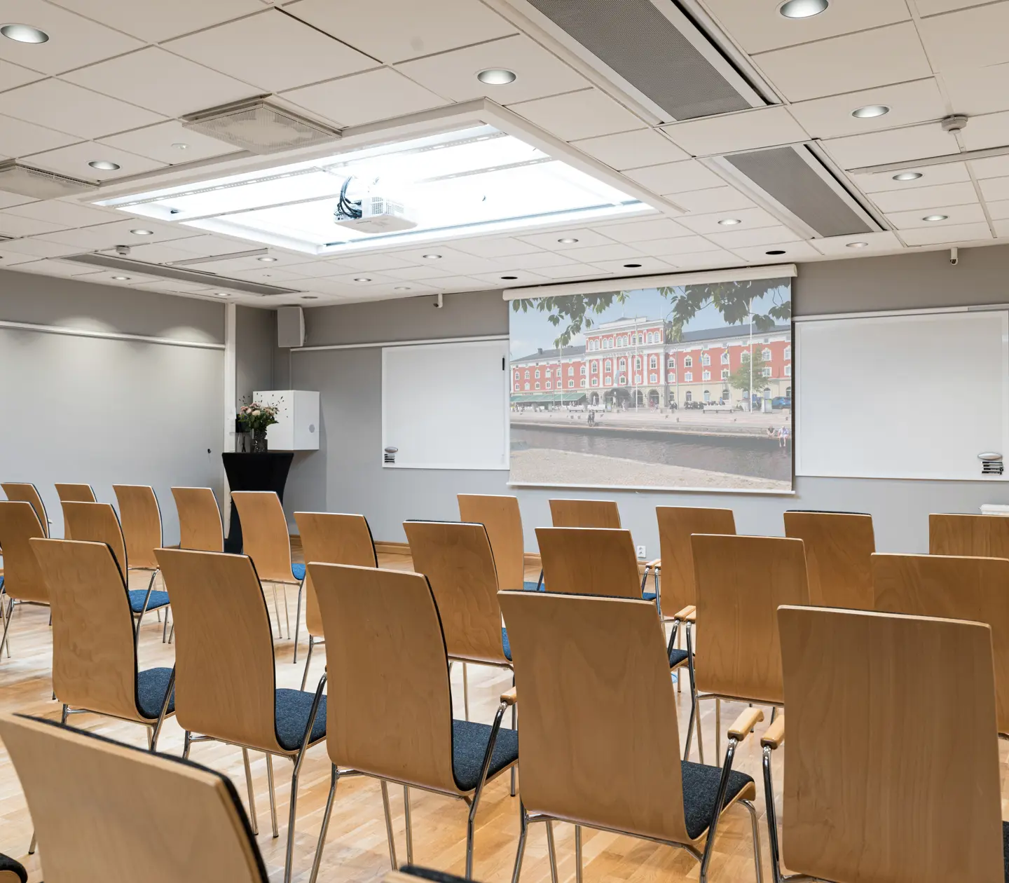 Modern conference room with rows of empty wooden chairs facing a large presentation screen and whiteboard, ideal for business meetings and seminars.