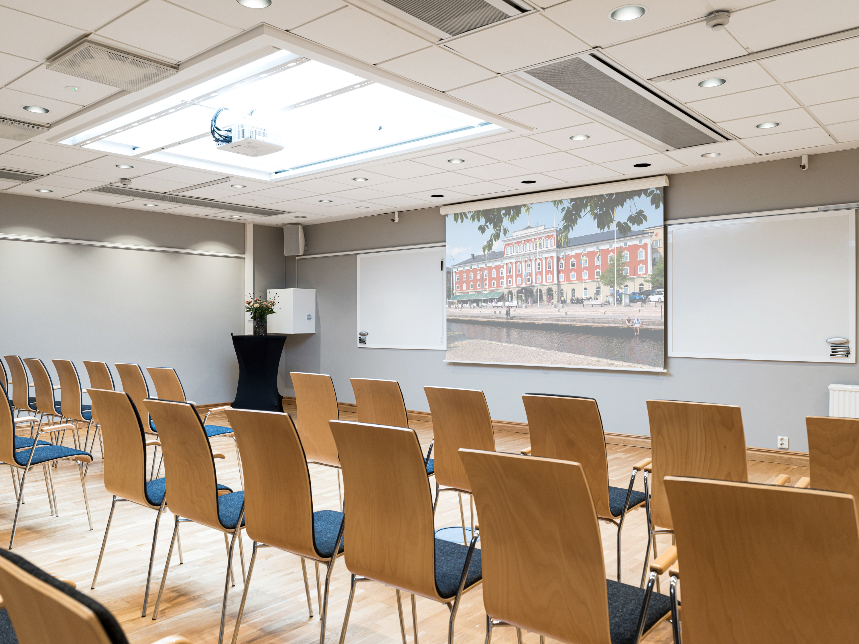 Modern conference room with rows of wooden chairs facing a screen displaying a large building.