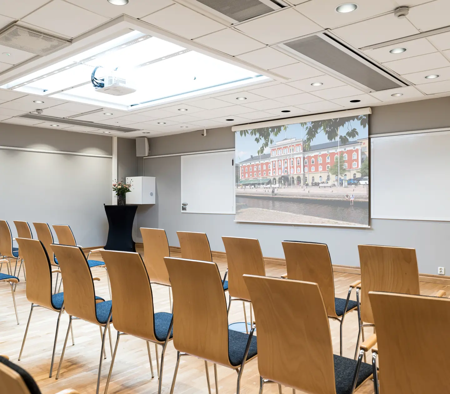 Modern conference room with rows of wooden chairs facing a screen displaying a large building.
