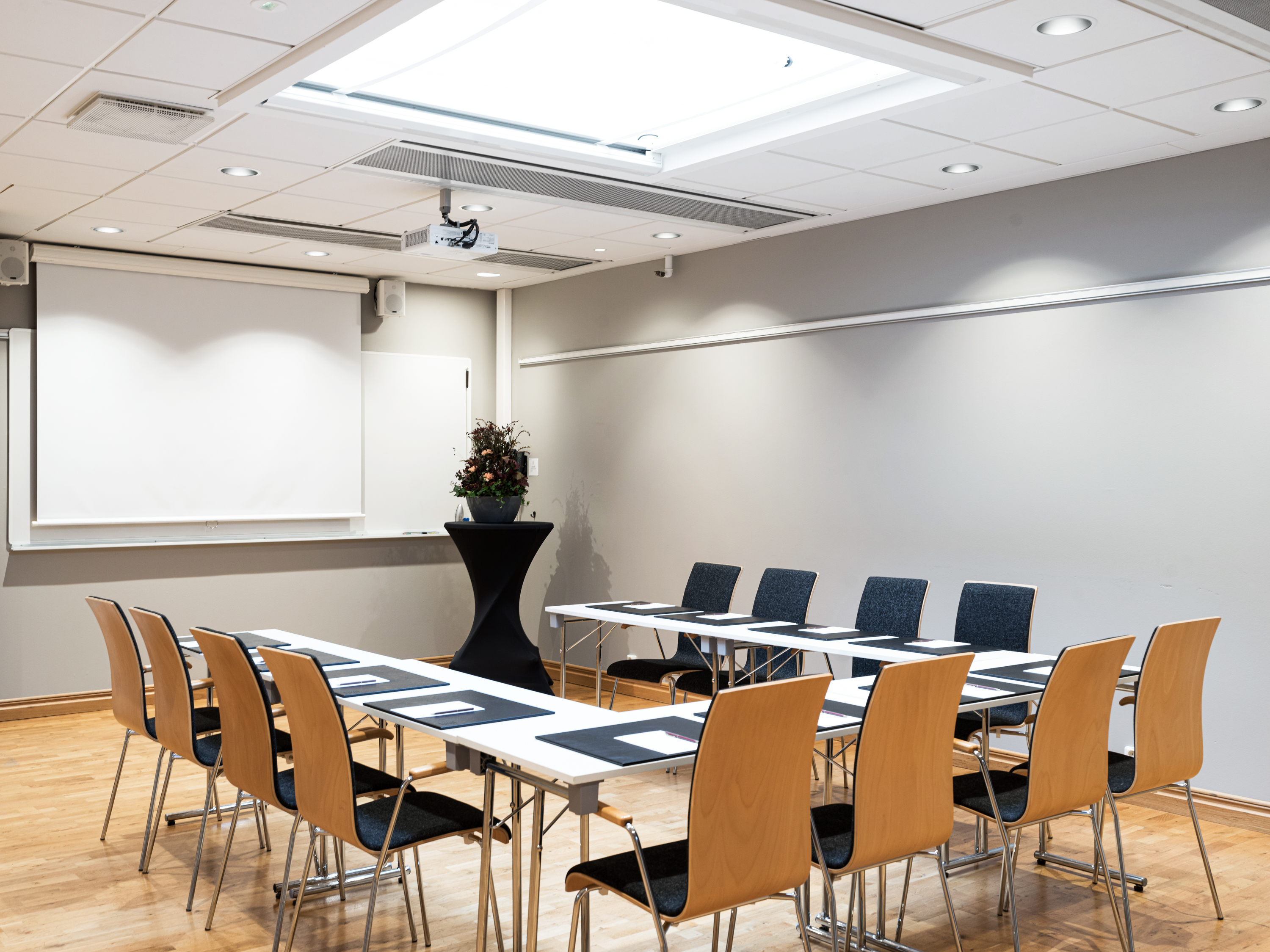 Modern conference room setup with wooden chairs, rectangular tables, and a projector screen, designed for business meetings or presentations.