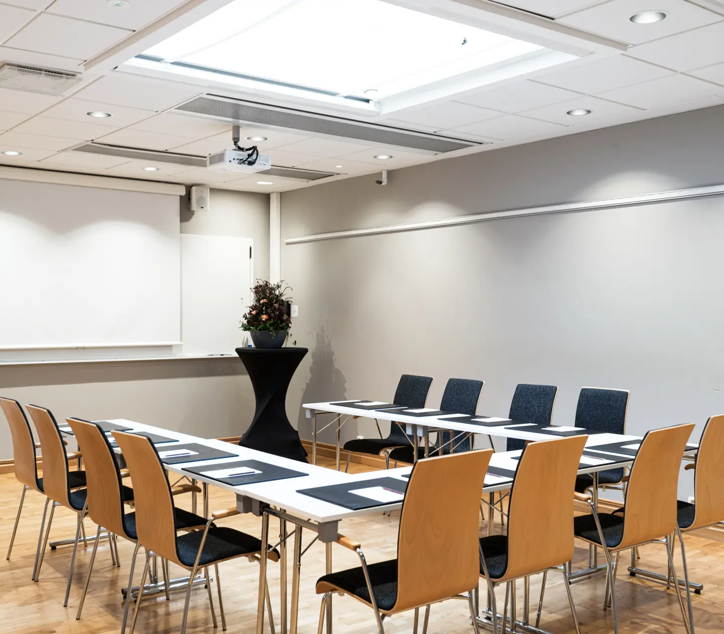 Modern conference room setup with wooden chairs, rectangular tables, and a projector screen, designed for business meetings or presentations.