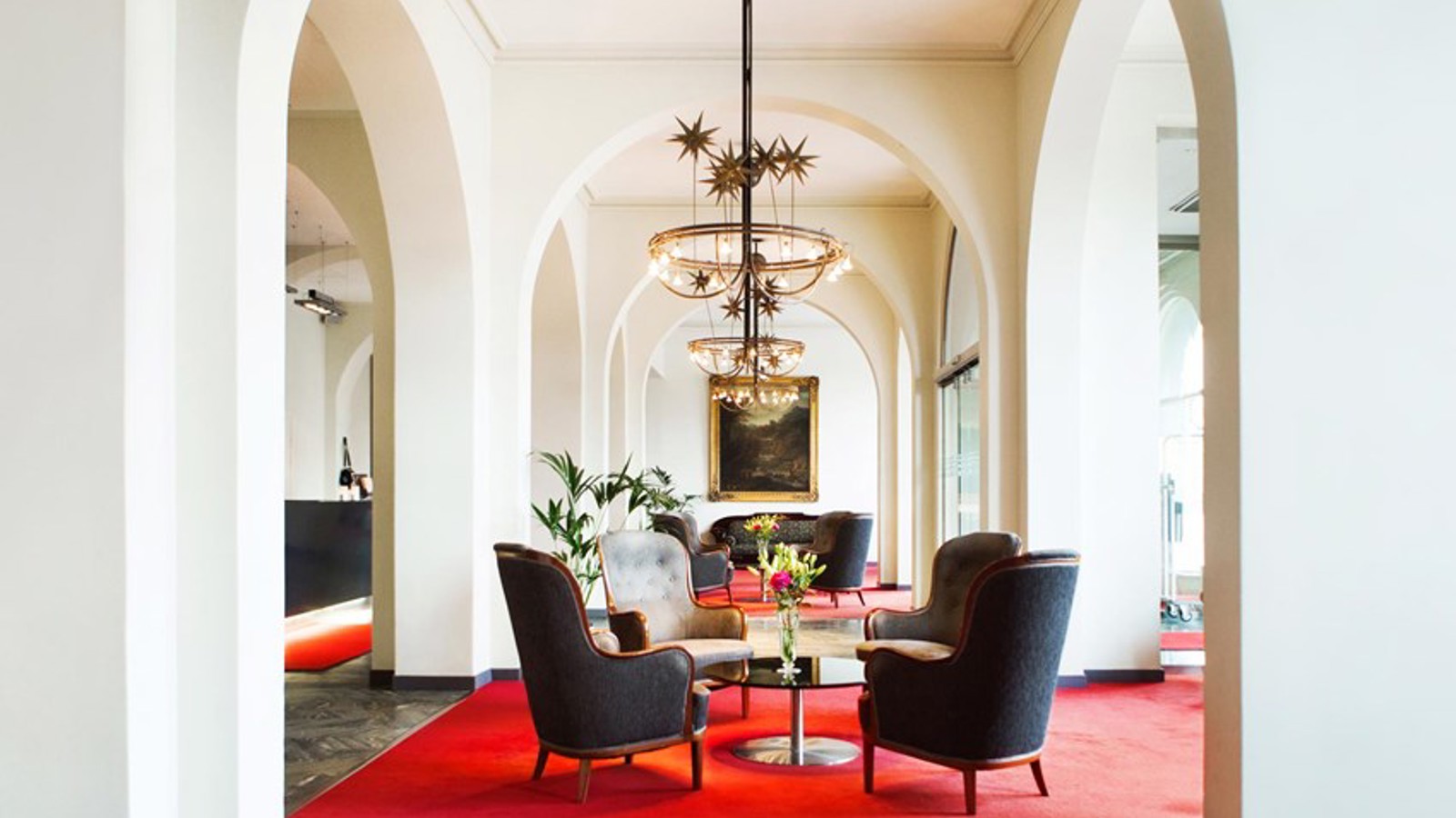 Light room with armchairs, white walls, red rug and arched doorways