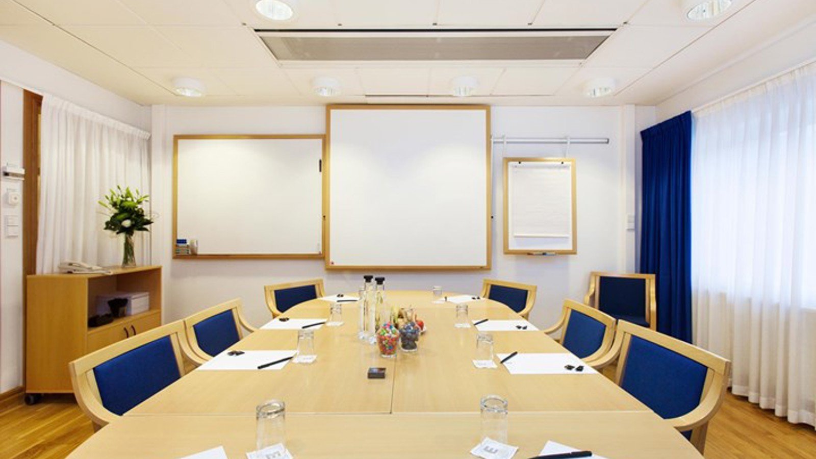 Ljust konferensrum med styrelsesittning, vita väggar, parkett och trämöbler