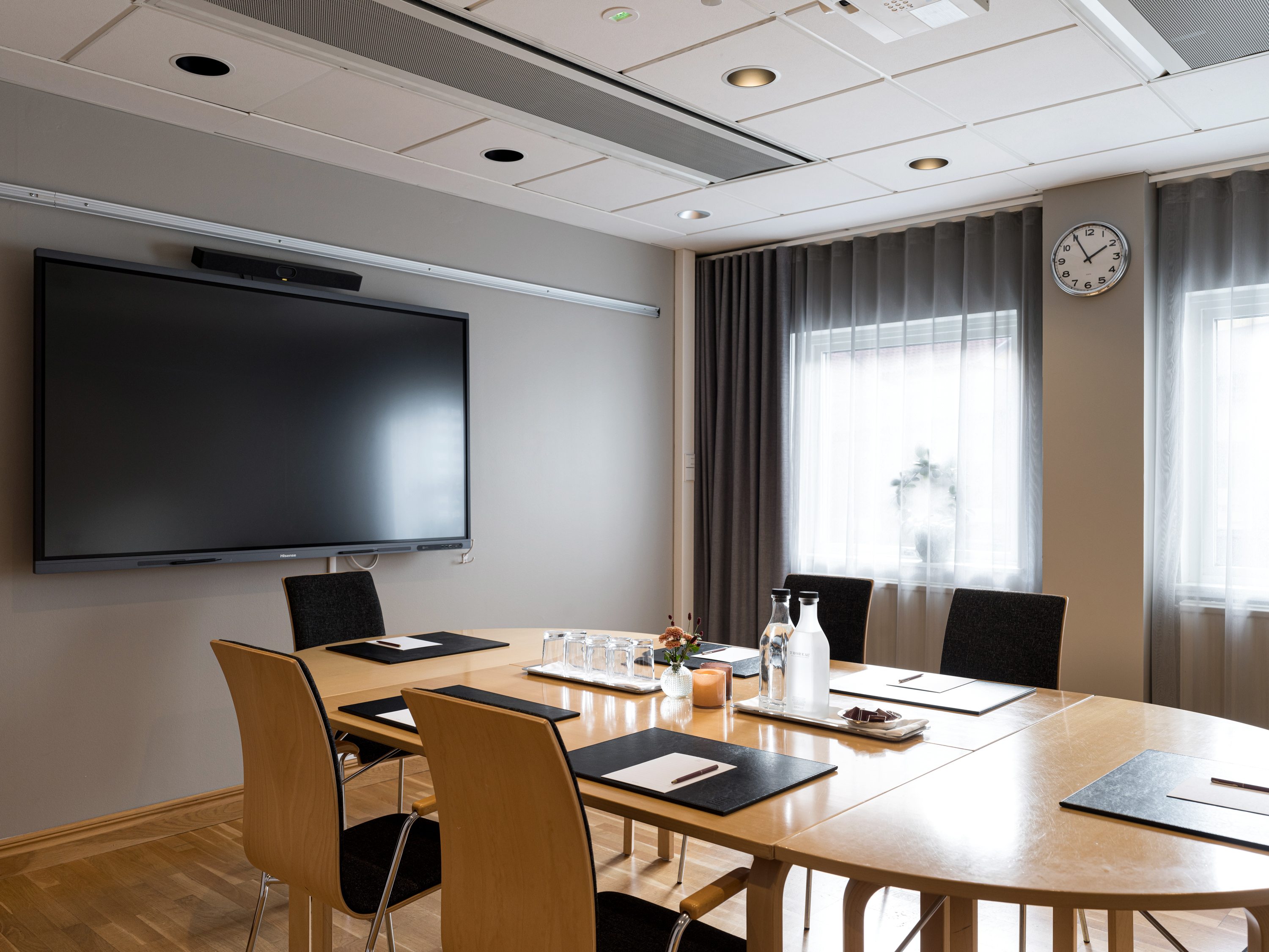 Modern conference room with a large screen, table, chairs, and natural lighting through sheer curtains, optimized for business meetings.