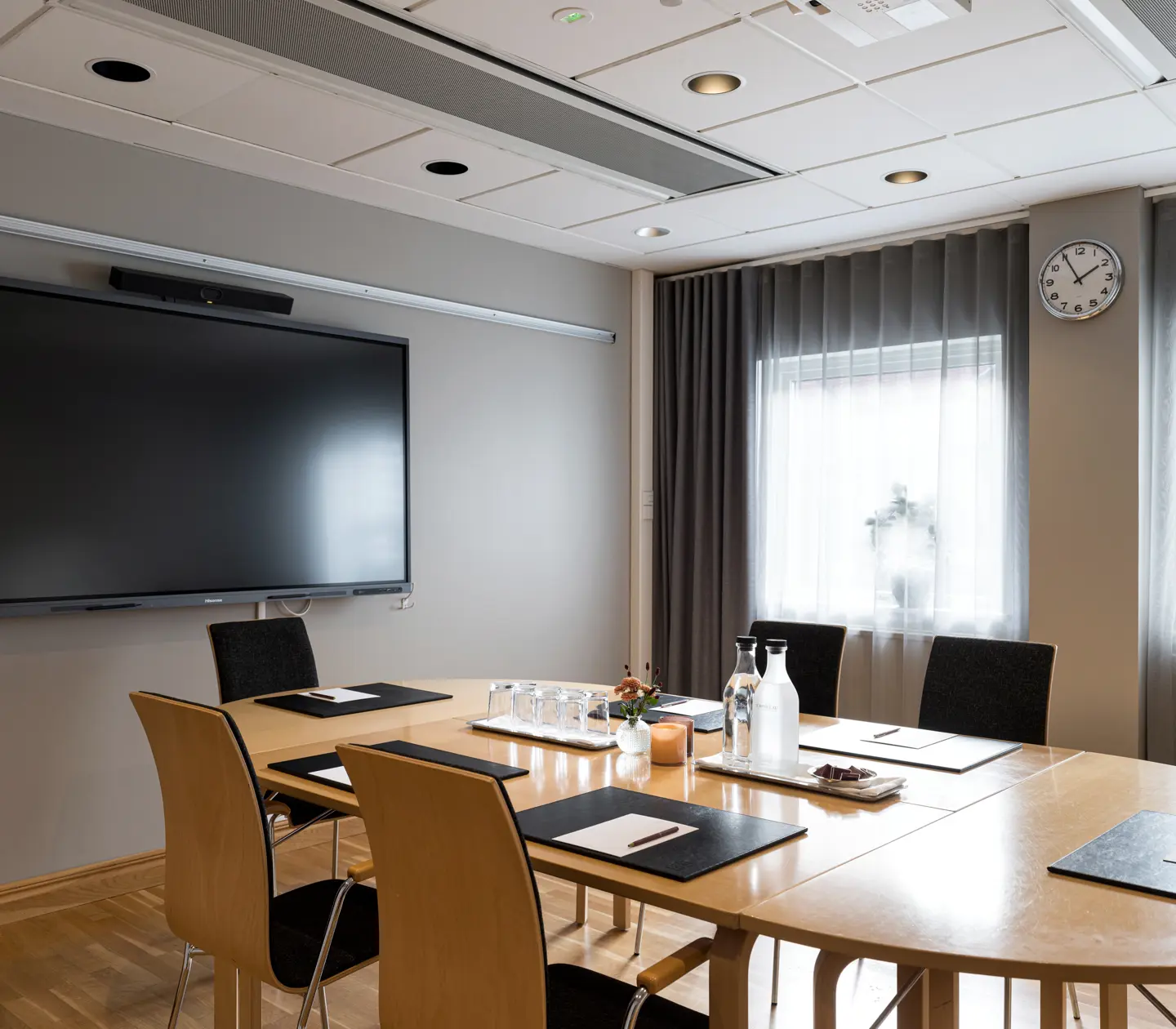 Modern conference room with a large screen, table, chairs, and natural lighting through sheer curtains, optimized for business meetings.