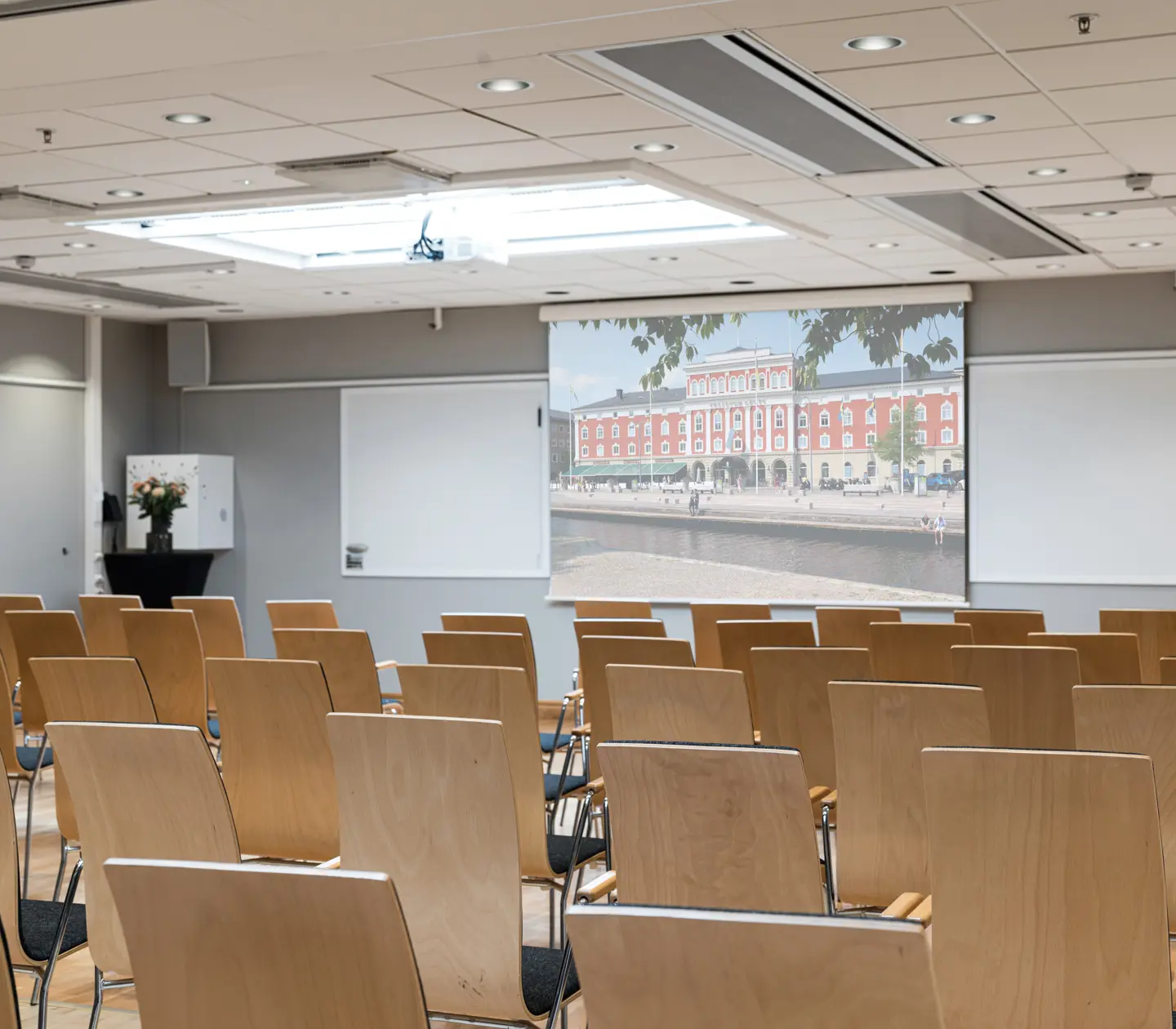 Conference room with wooden chairs and a large screen displaying a cityscape.