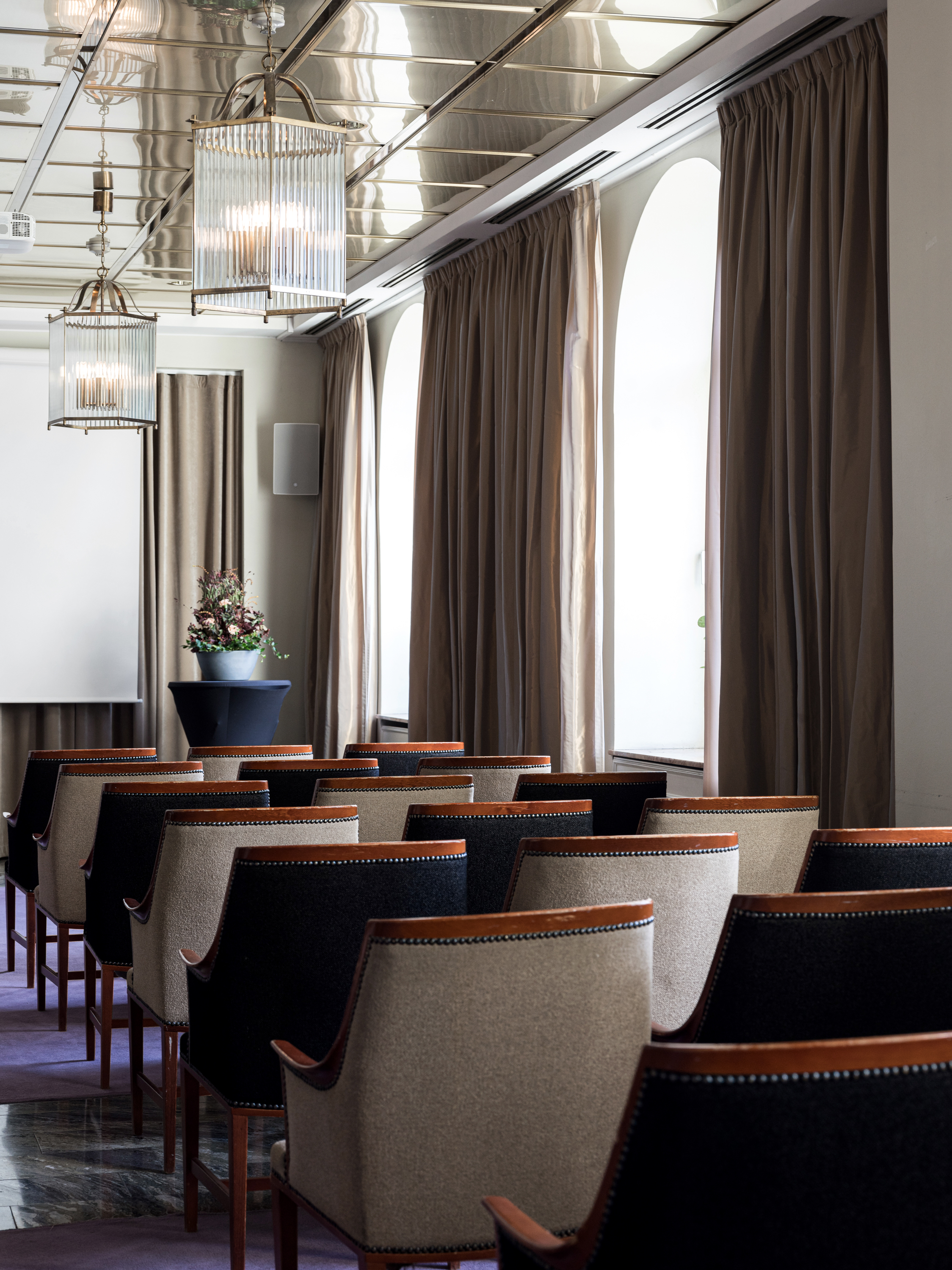 Conference room interior with rows of elegant chairs, a large window with curtains, and modern lighting.